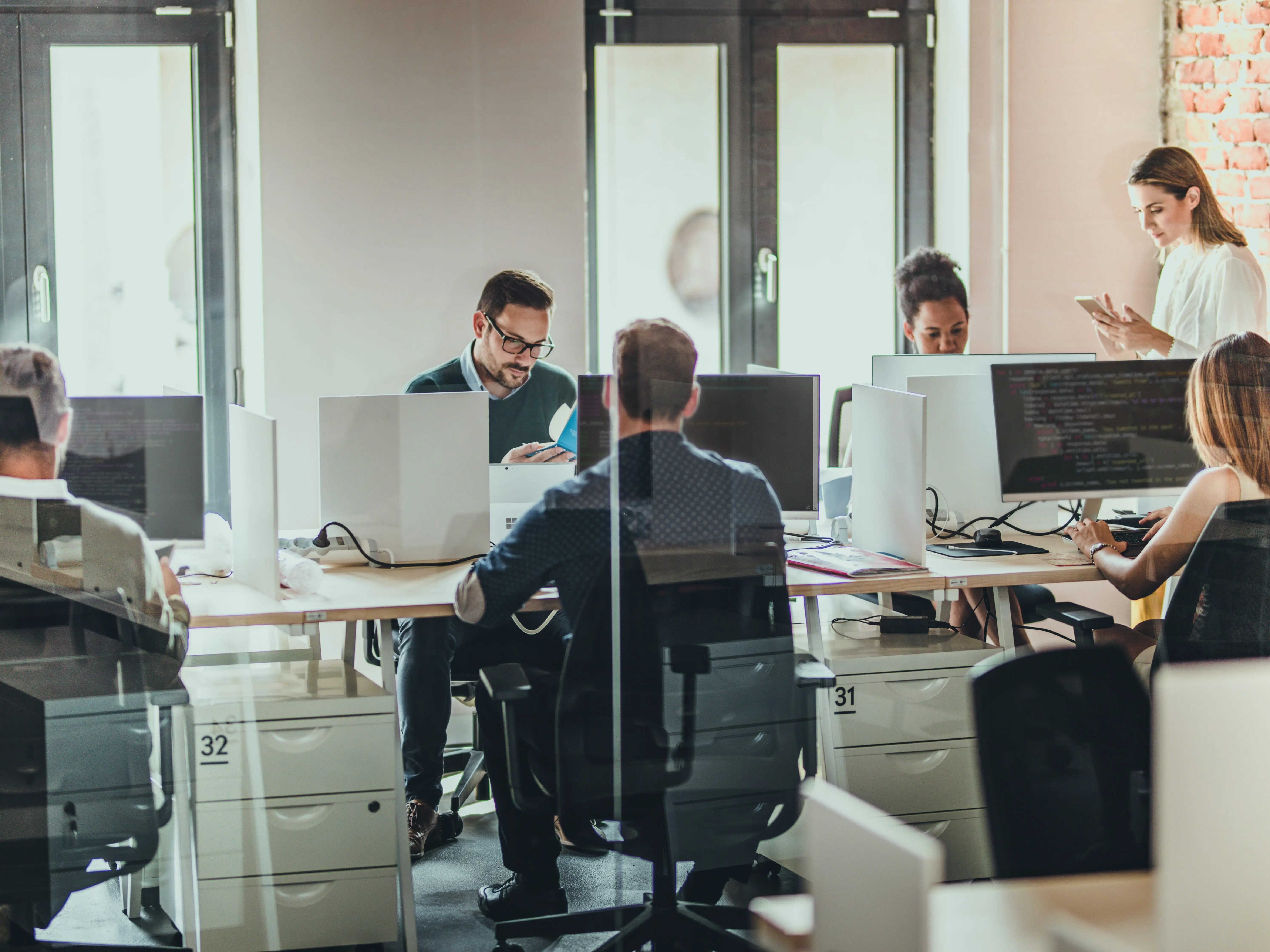 A group of people sitting at desks facing each other in an office while working on their computers.