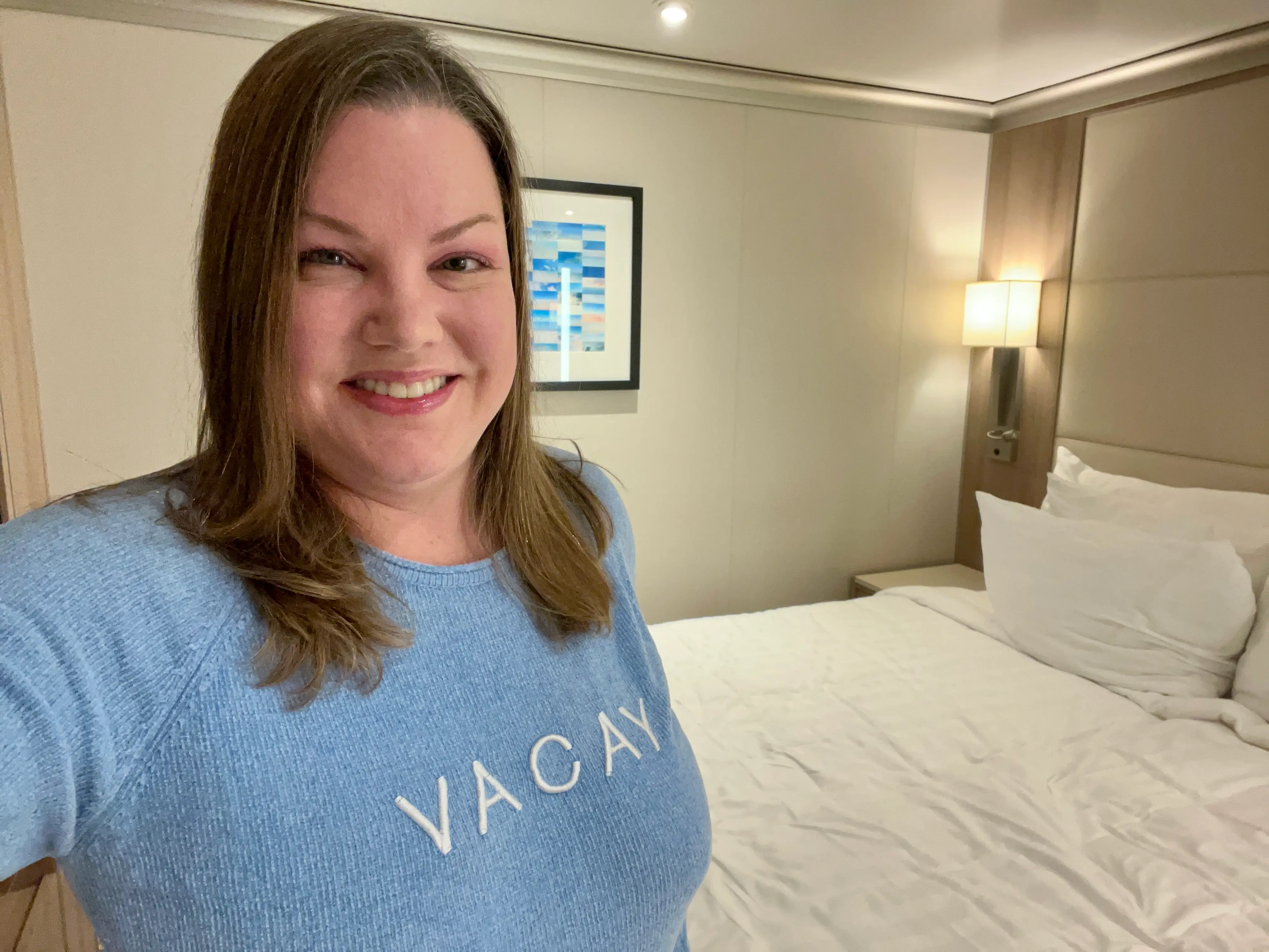A woman smiling and taking a selfie in a cruise cabin.