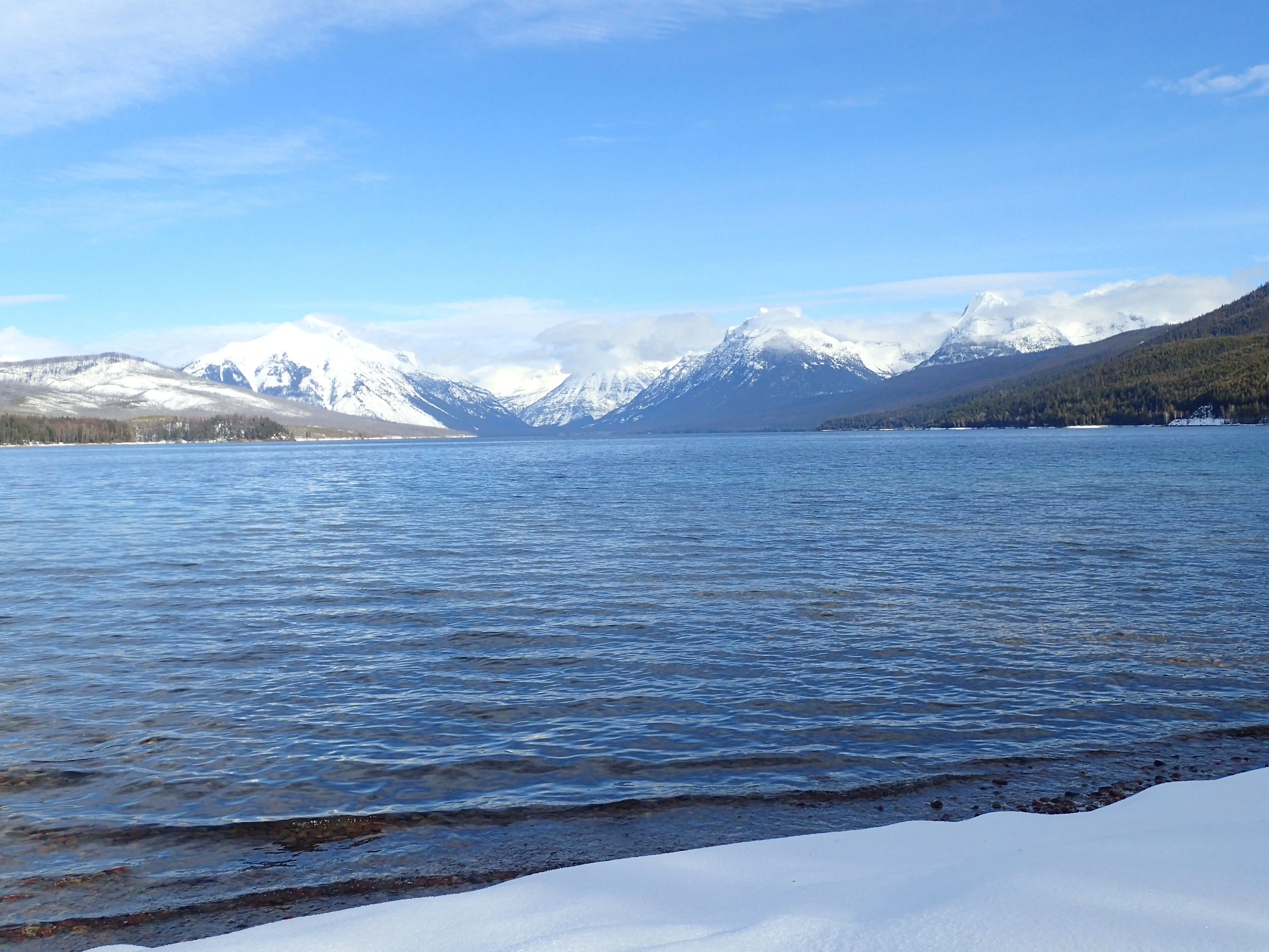 Snow-covered mountains surround a lake with snowy shores.