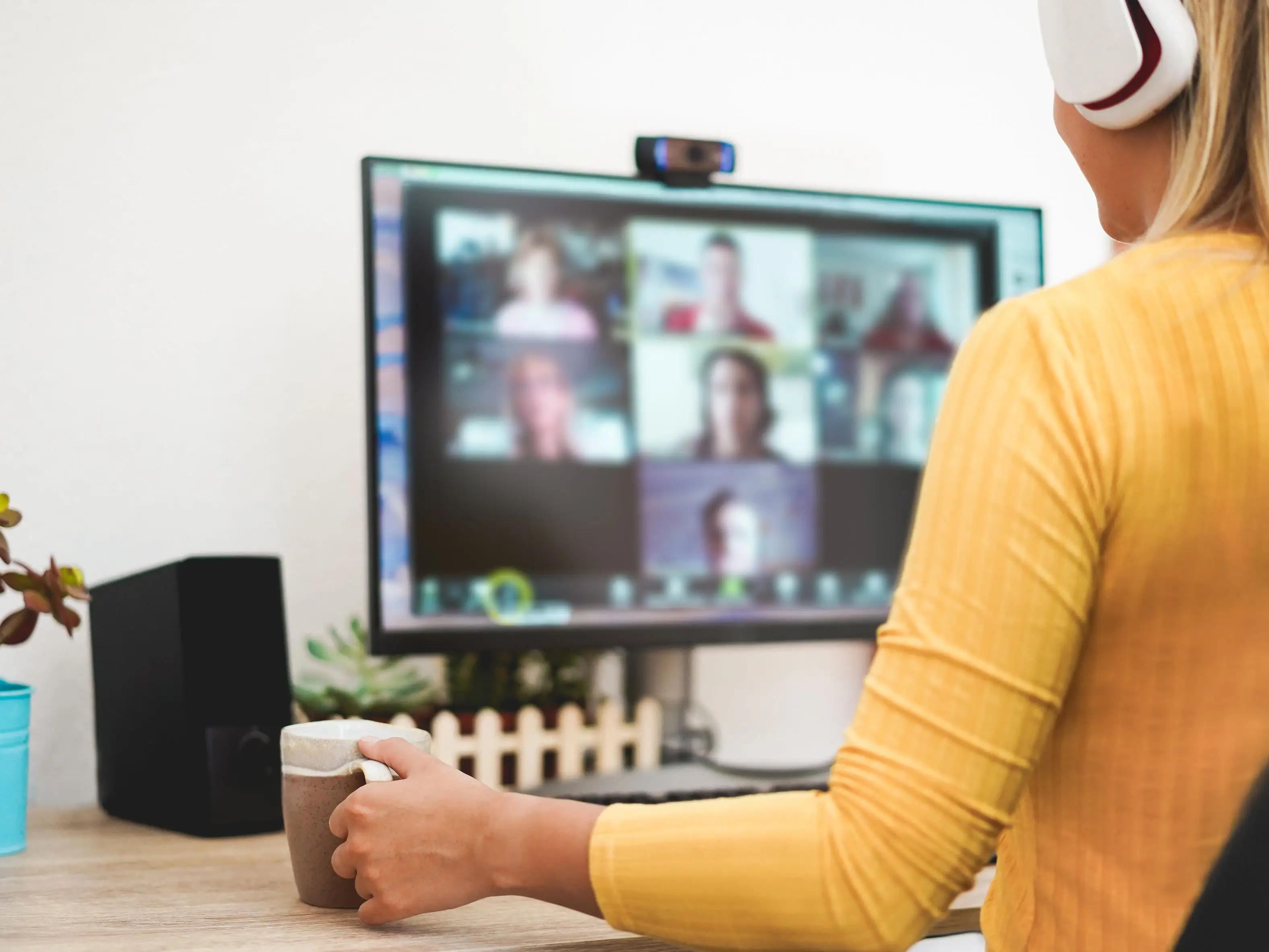 A woman in a yellow shirt with white headphones on a video call.
