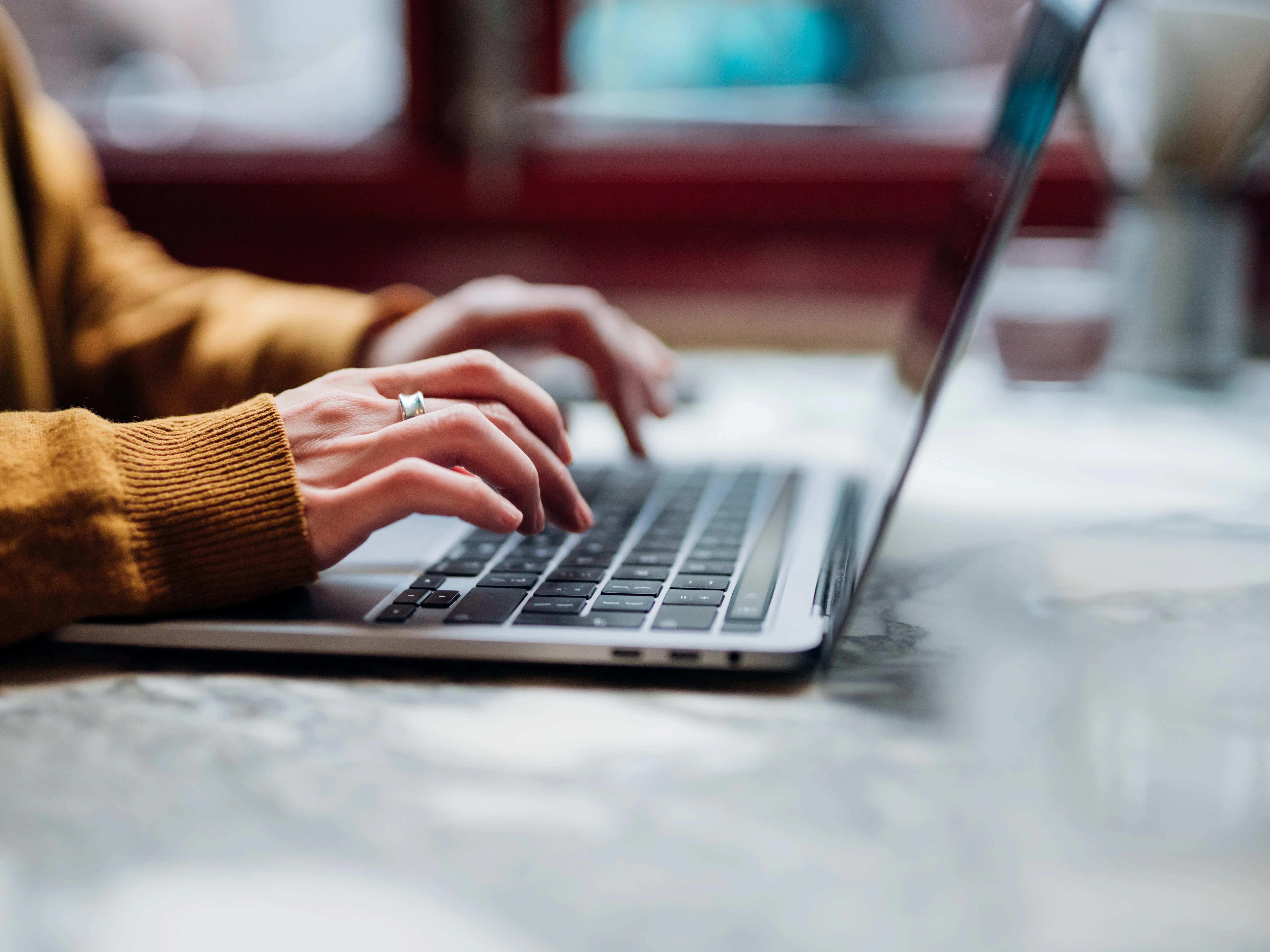 A woman in a beige sweater typing at a laptop.