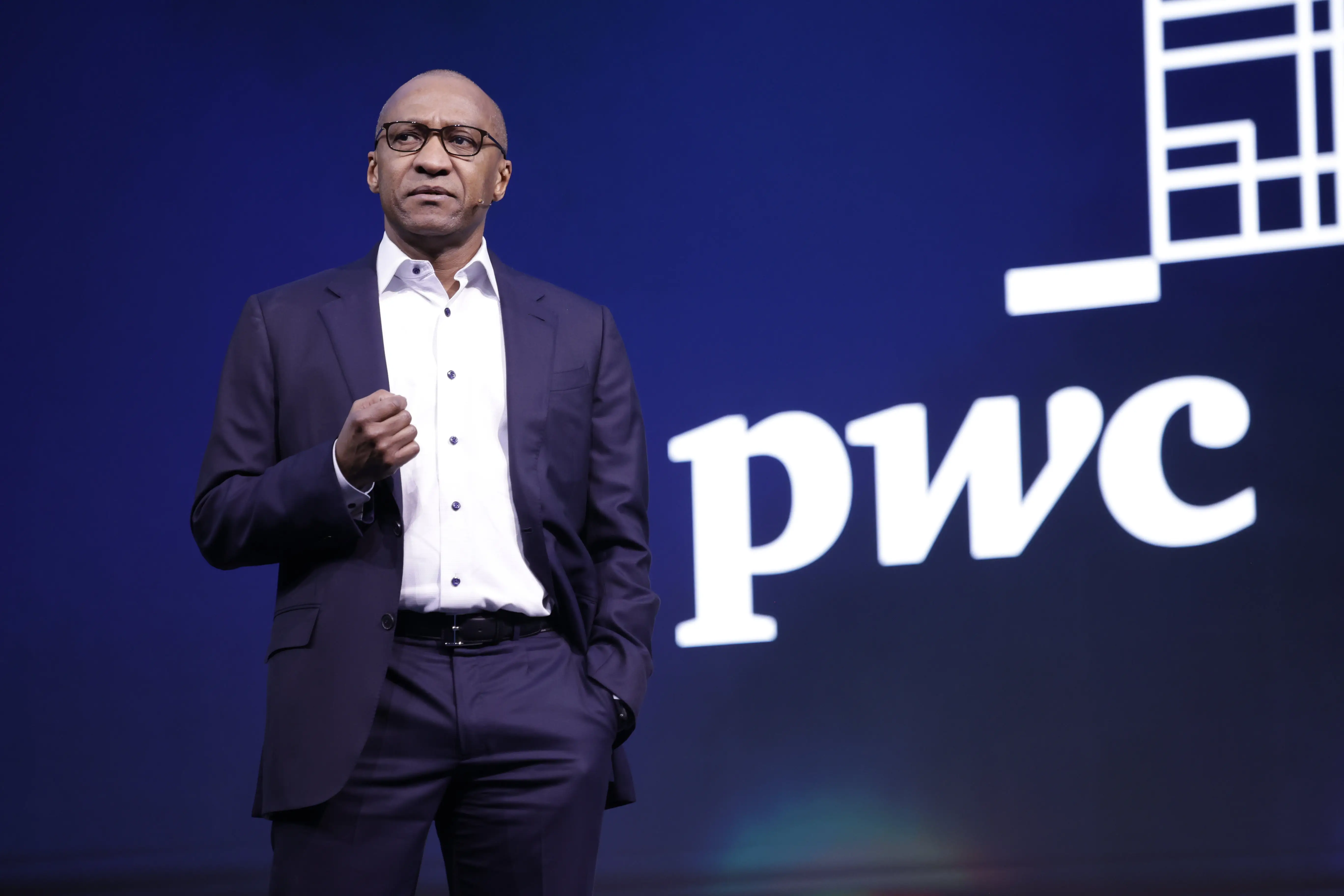 Mohamed Kande speaking at an event with the PwC logo behind him.