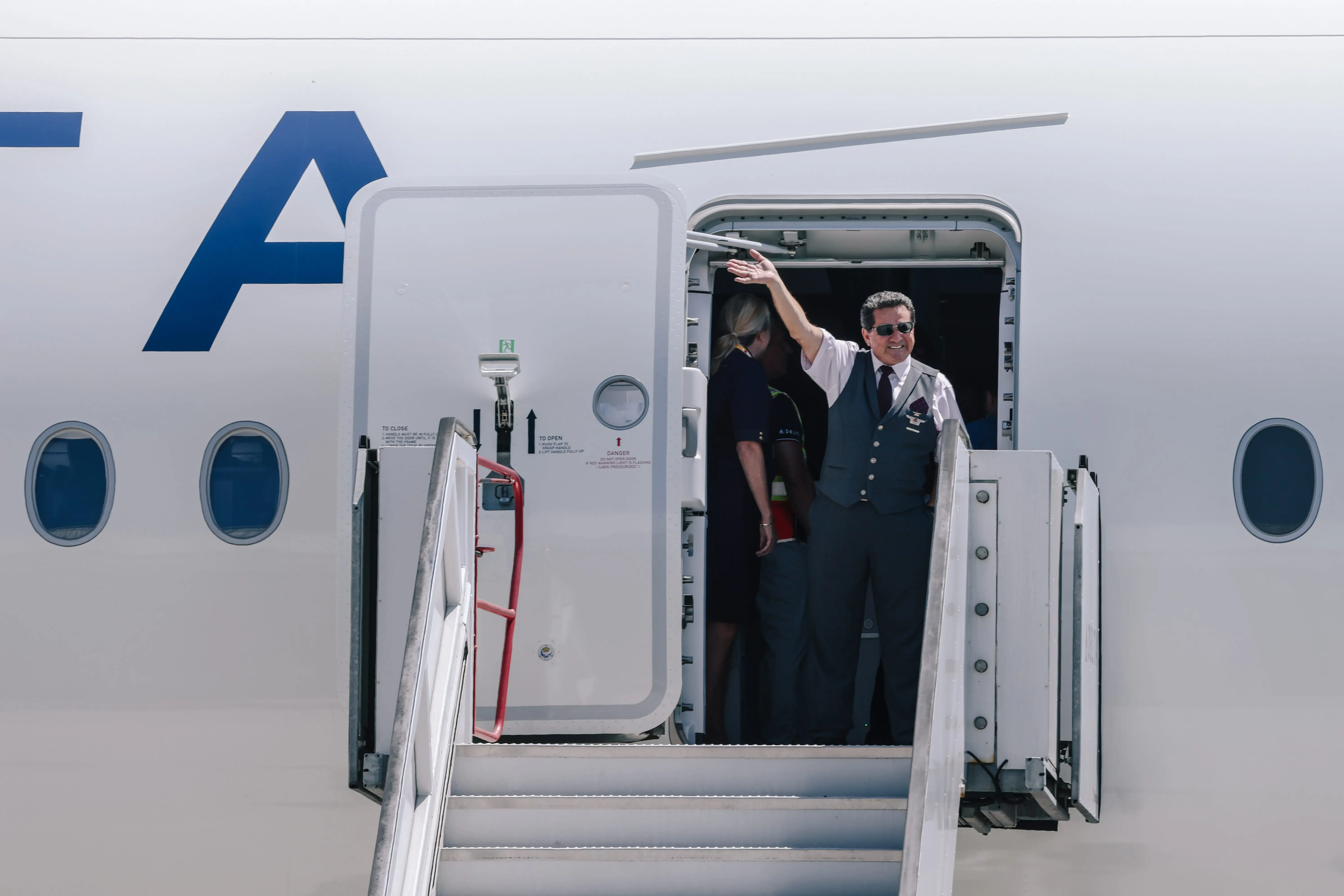 A Delta Airlines flight attendant waves from atop the boarding stairs.