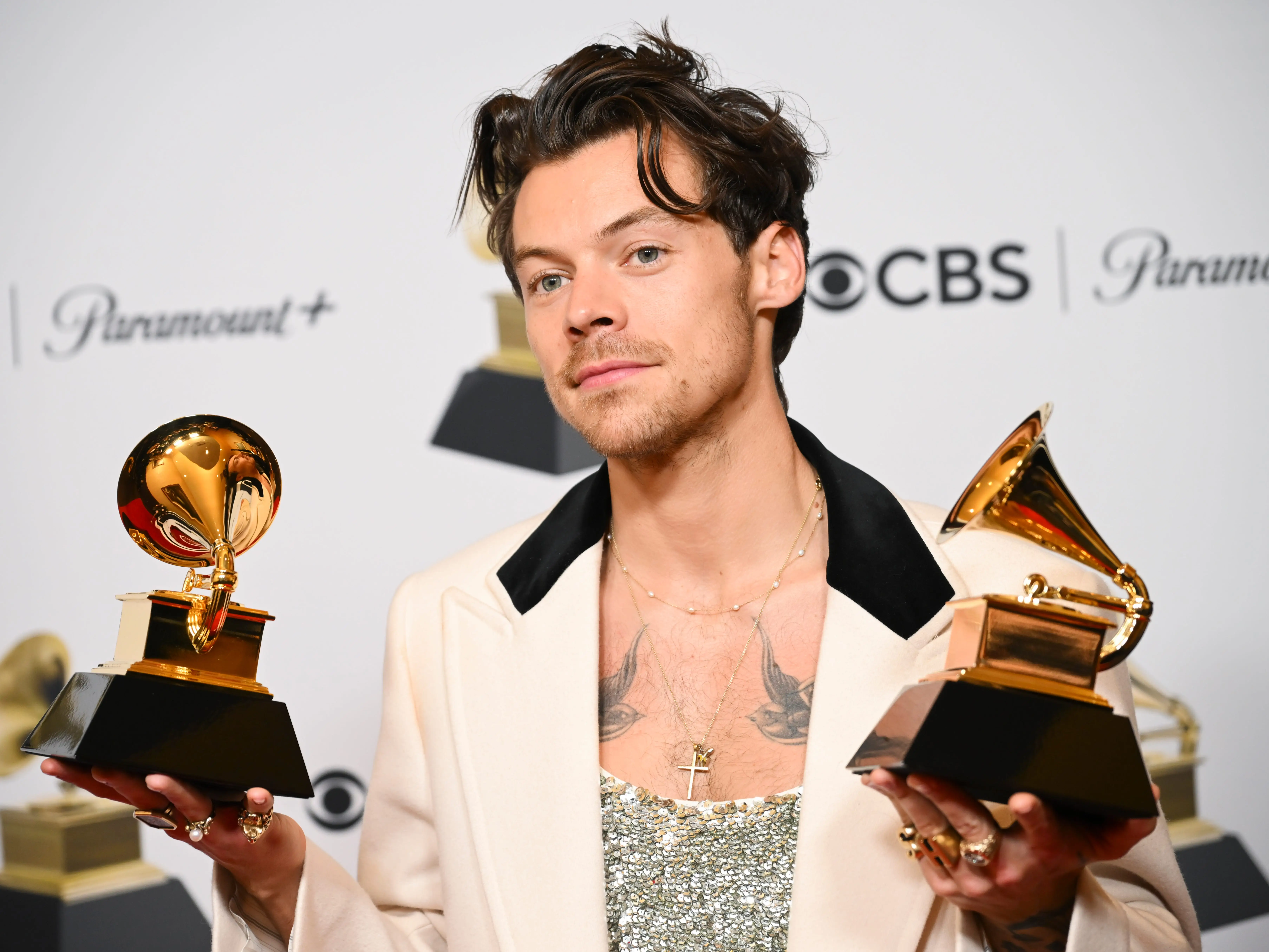 harry styles holding up two grammy awards on the red carpet