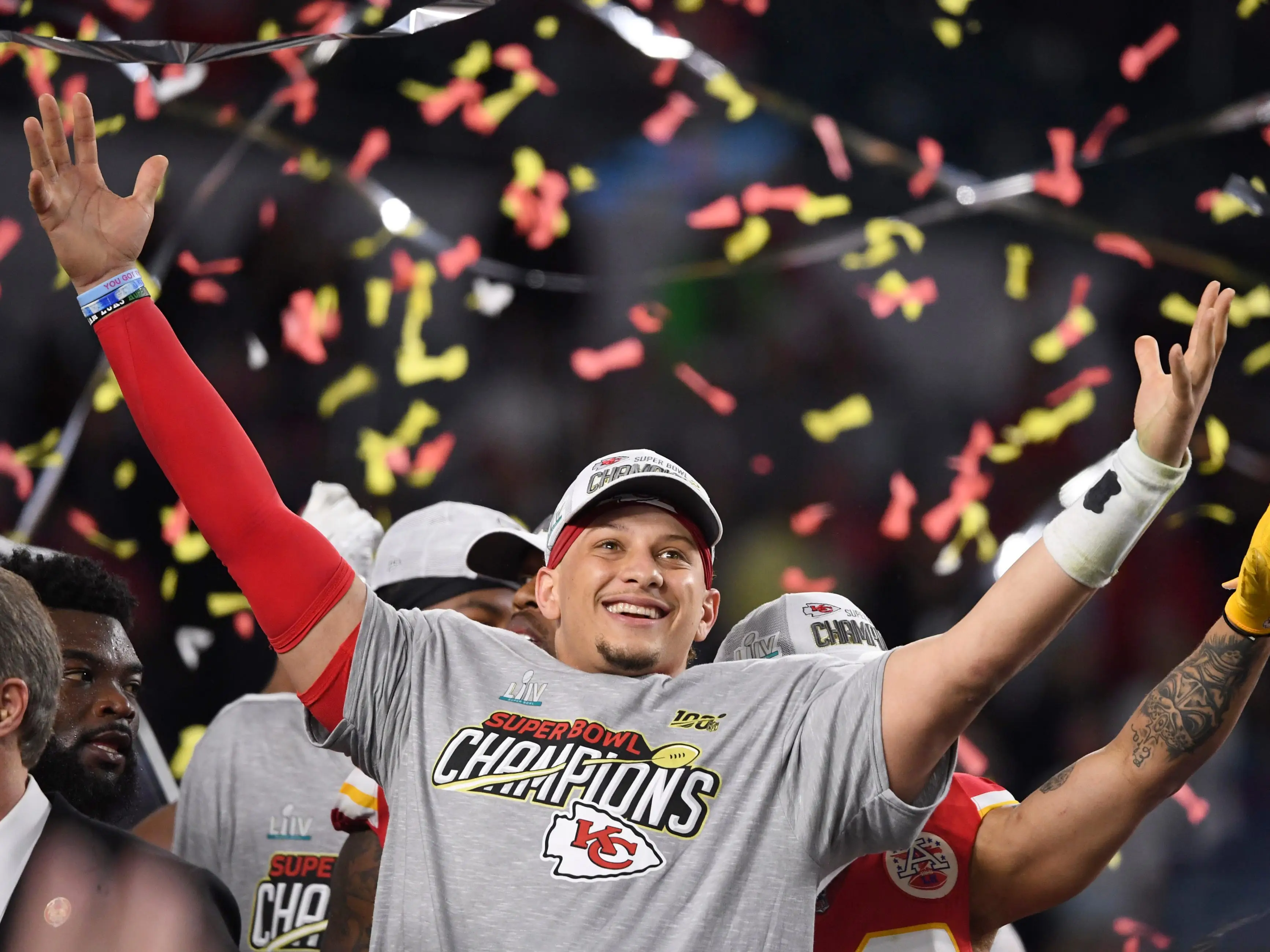 Patrick Mahomes stands with his arms raised, smiling as confetti falls around him following the Chiefs' Super Bowl LIV win.
