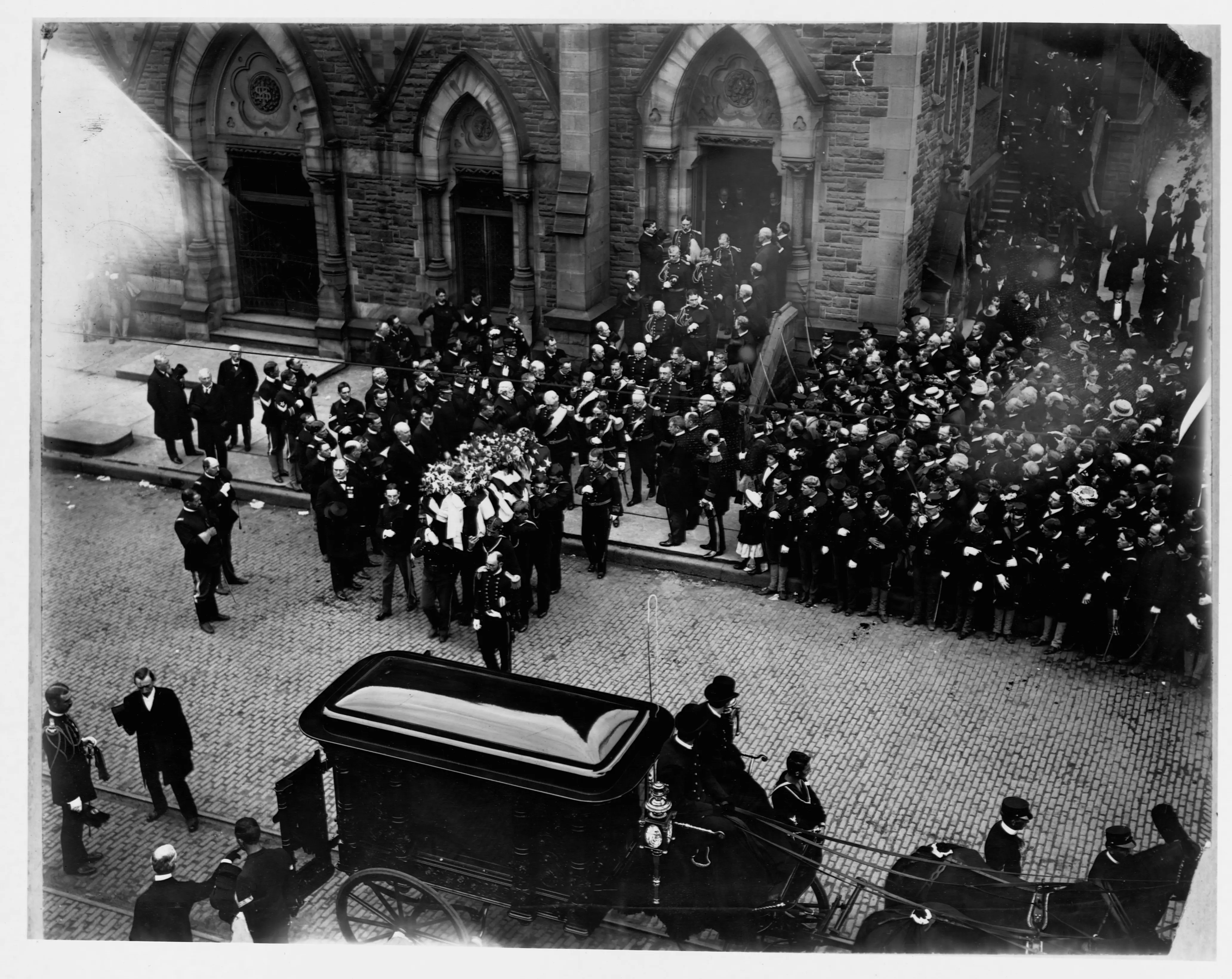 A crowd gathers on the street to watch the coffin of President William McKinley being transferred to a hearse after his funeral services.