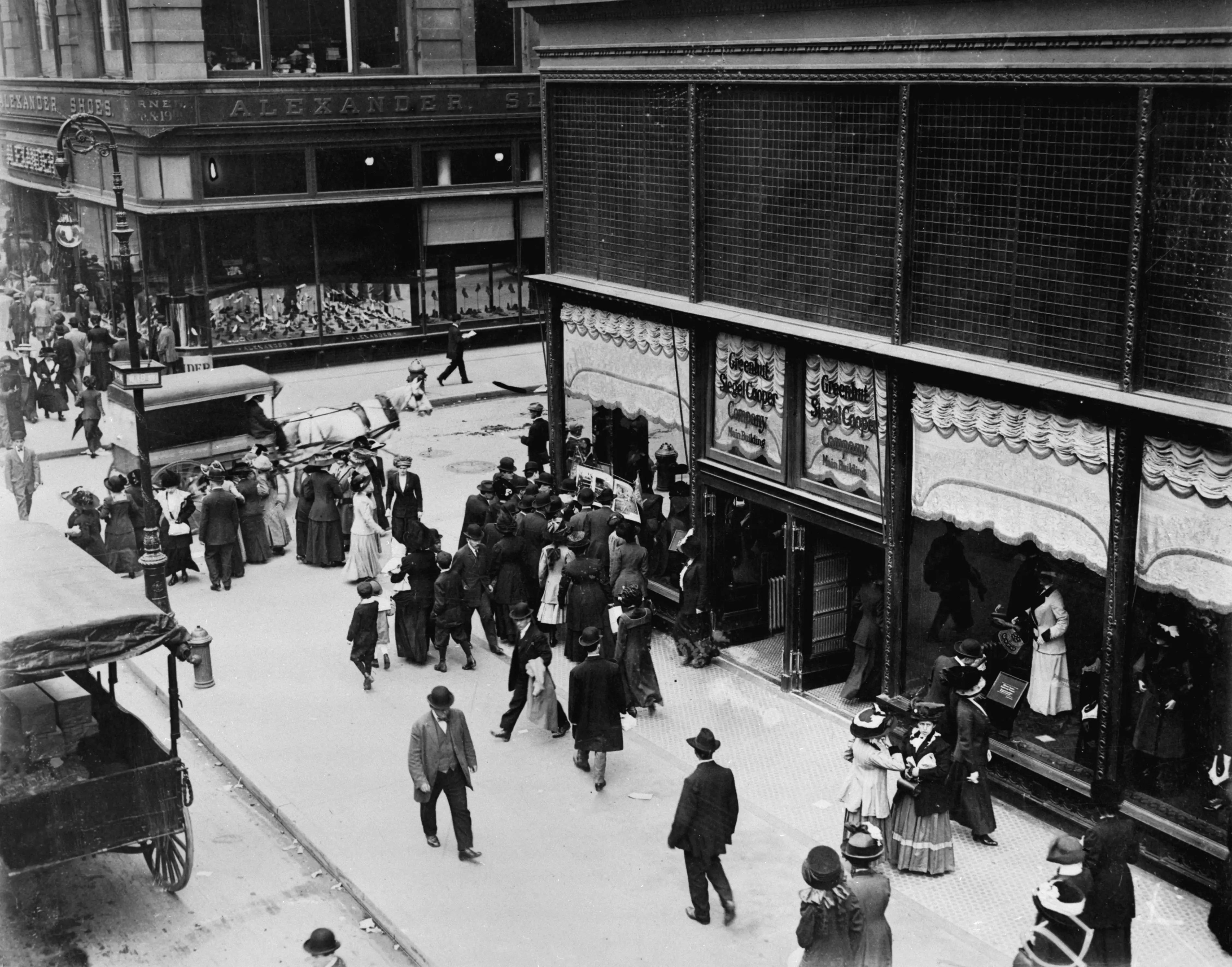 Siegel Cooper Department Store at corner of Sixth Avenue and West 19th Street on Ladies' Mile. A small crowd peers into window to read advertisement. ca. 1890s.