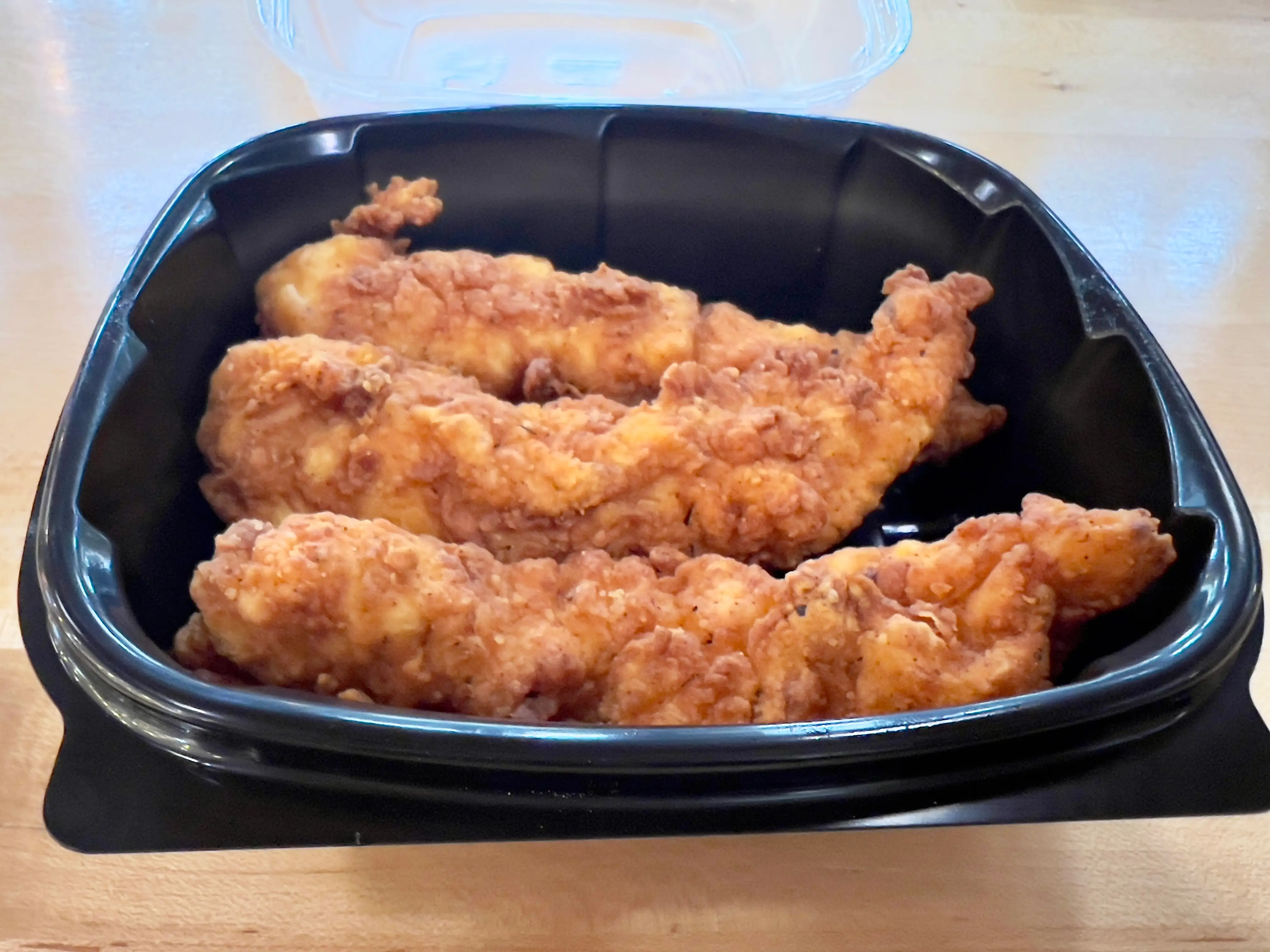 Three chicken tenders in a black plastic container.