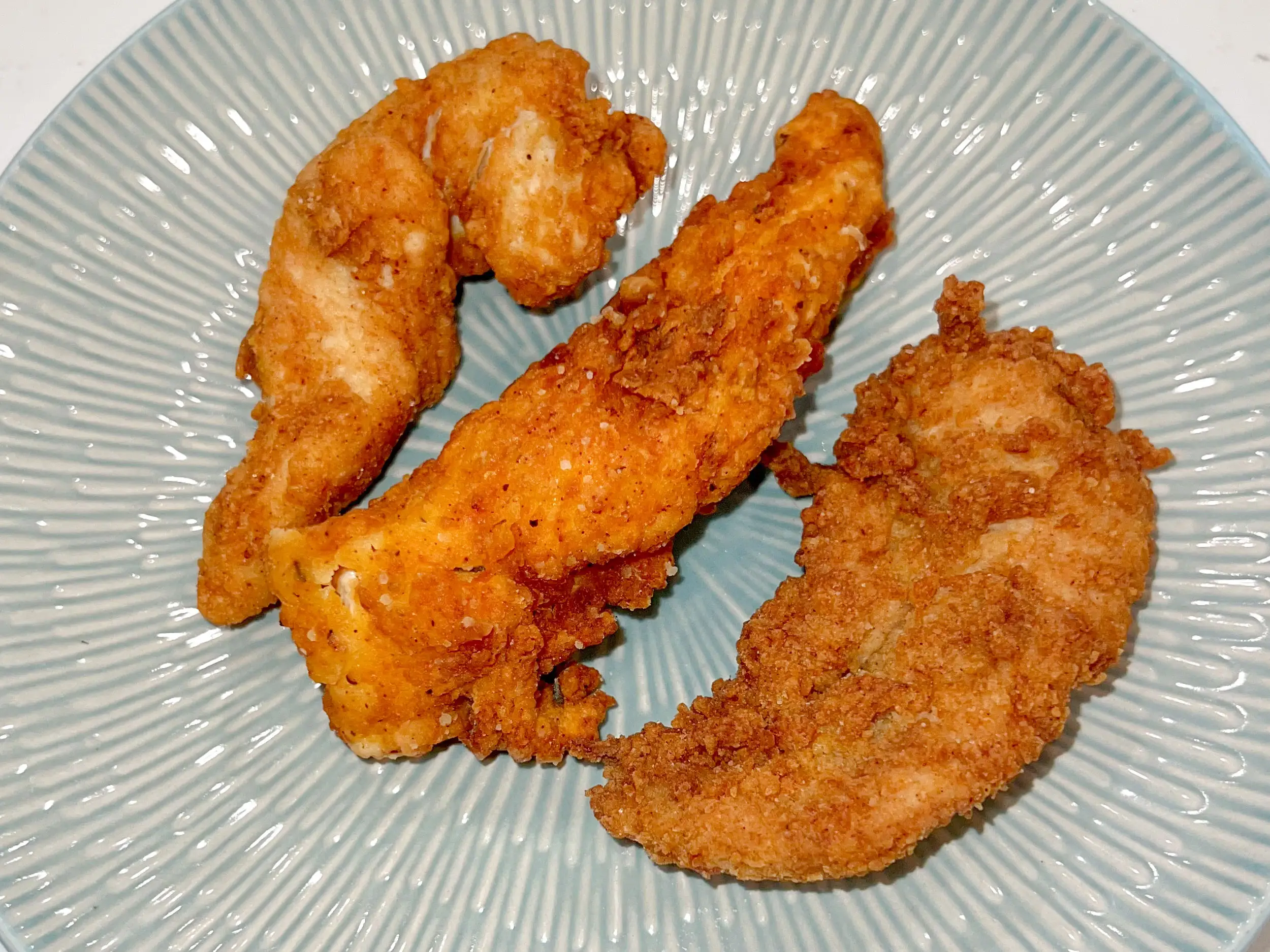 Three chicken tenders on a light green plate.