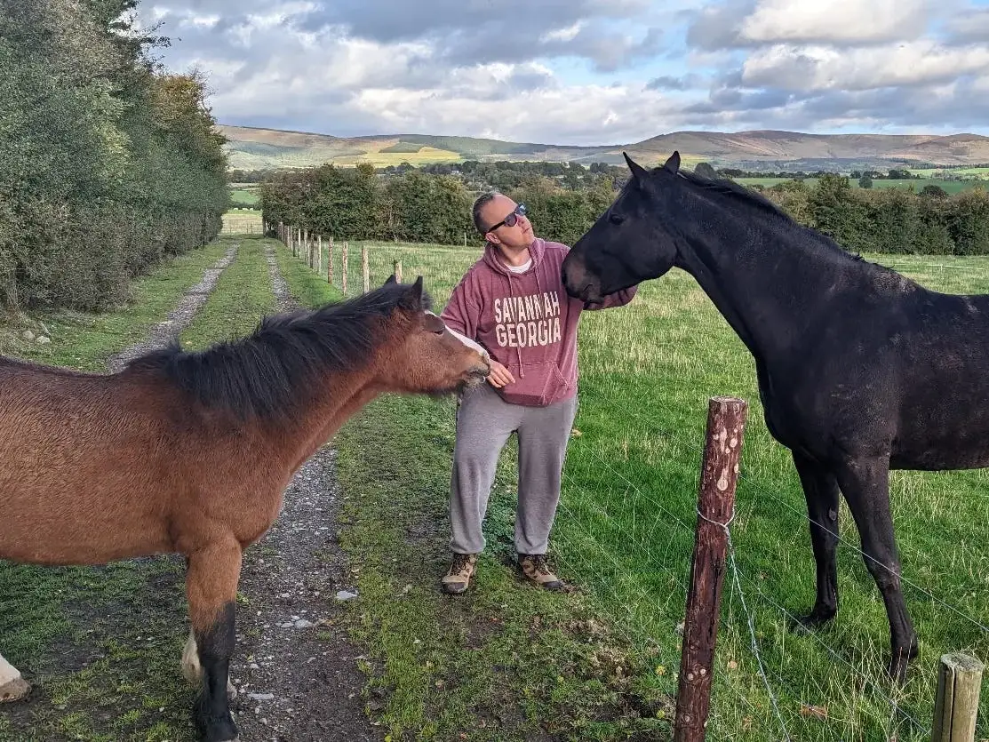Jason pets two horses on a farm in Ireland.