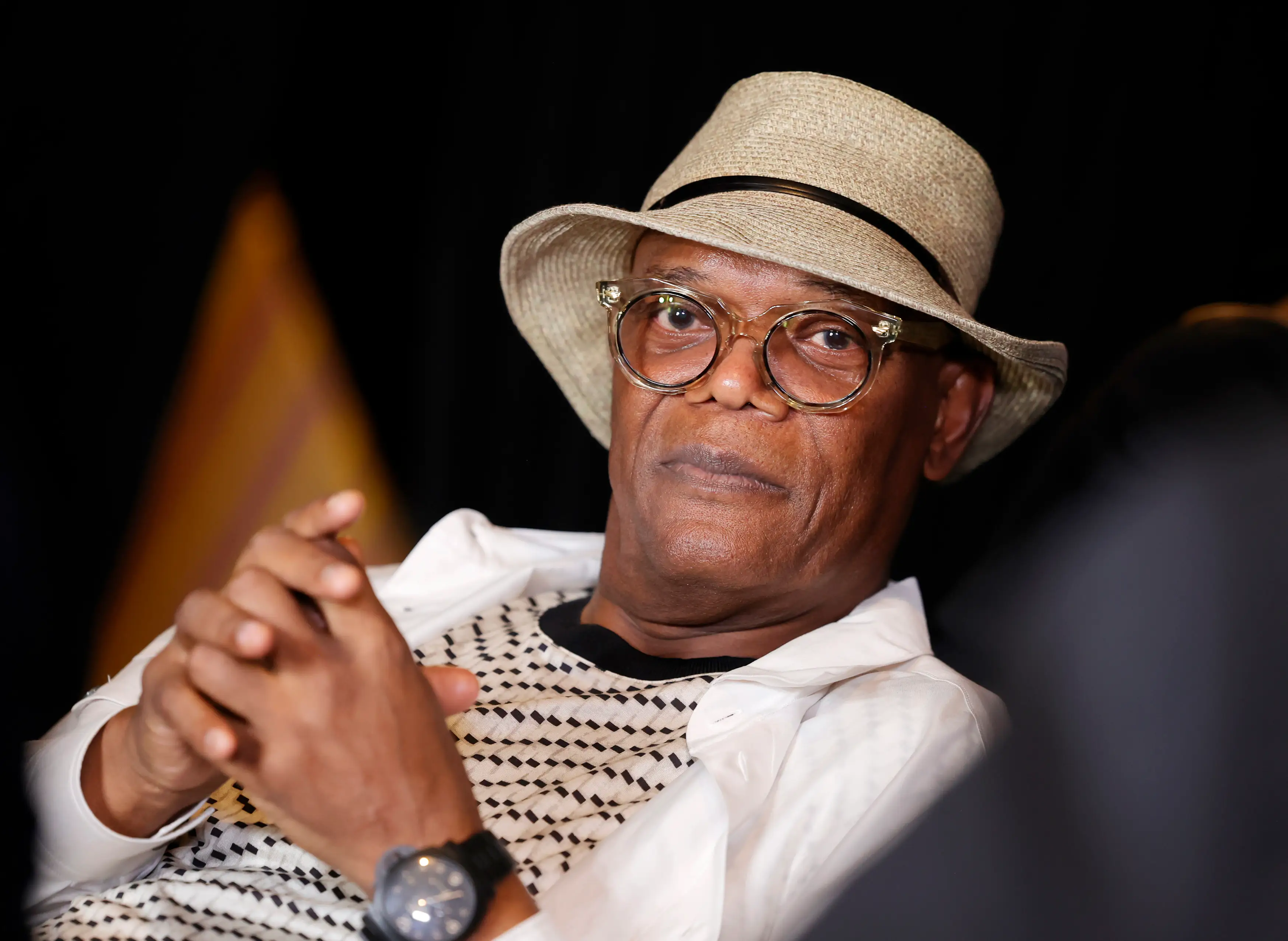 Samuel L. Jackson with hants folded wearing a hat