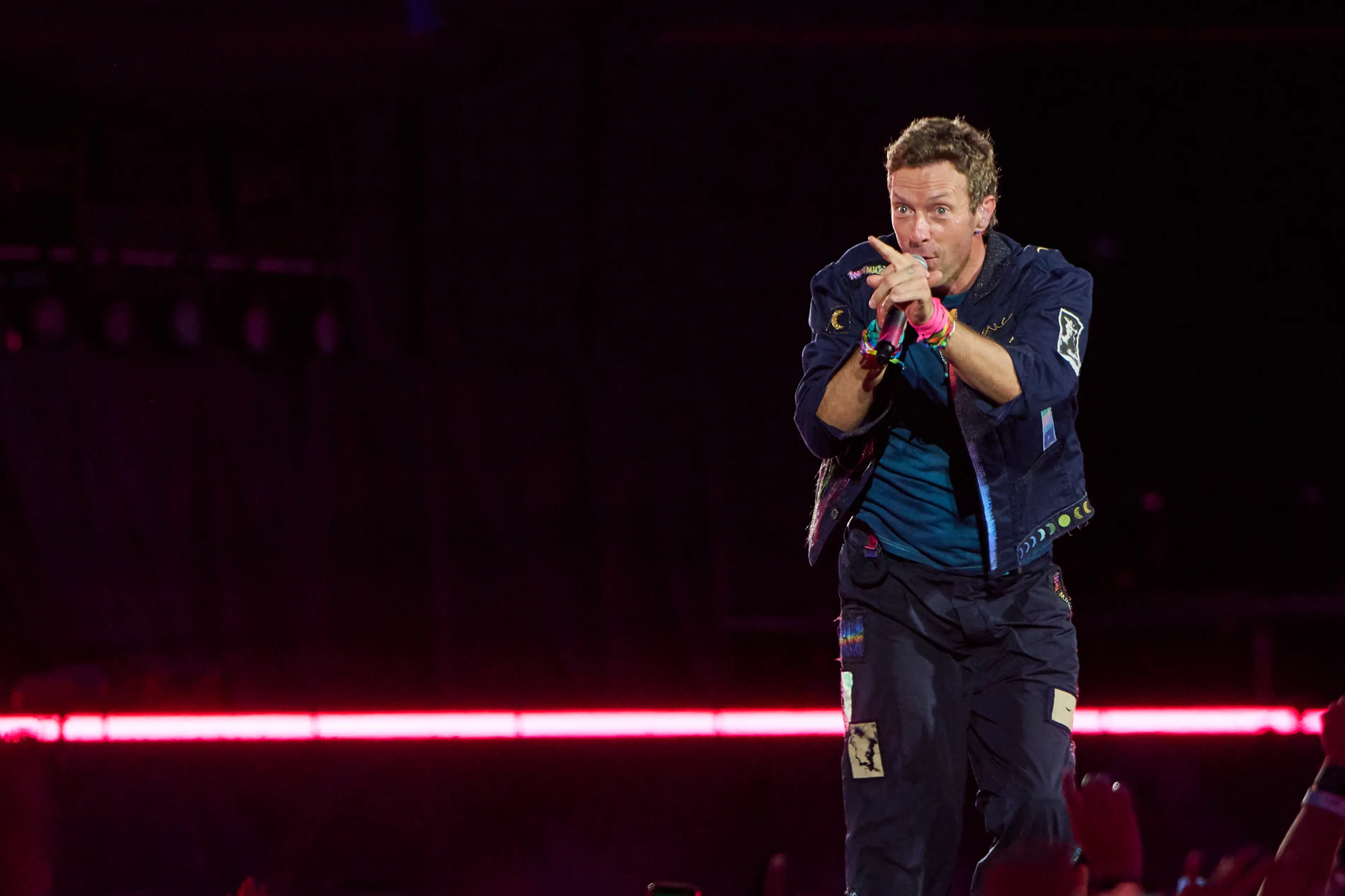 Chris Martin of Coldplay sings onstage pointing his finger at the crowd.