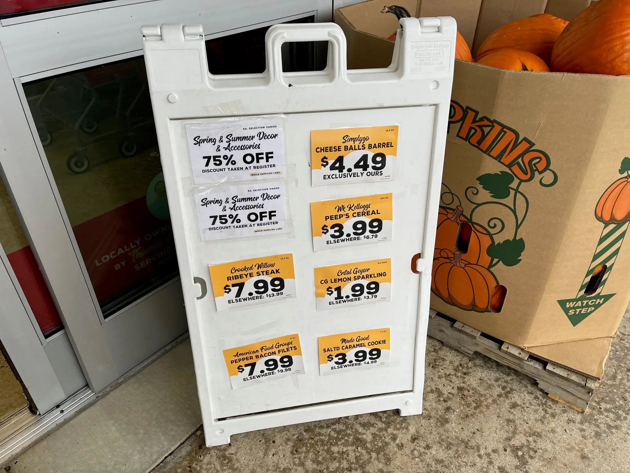 A sandwich-board sign outside a Grocery Outlet store shows featured sale items, such as cheese balls and ribeye steaks.