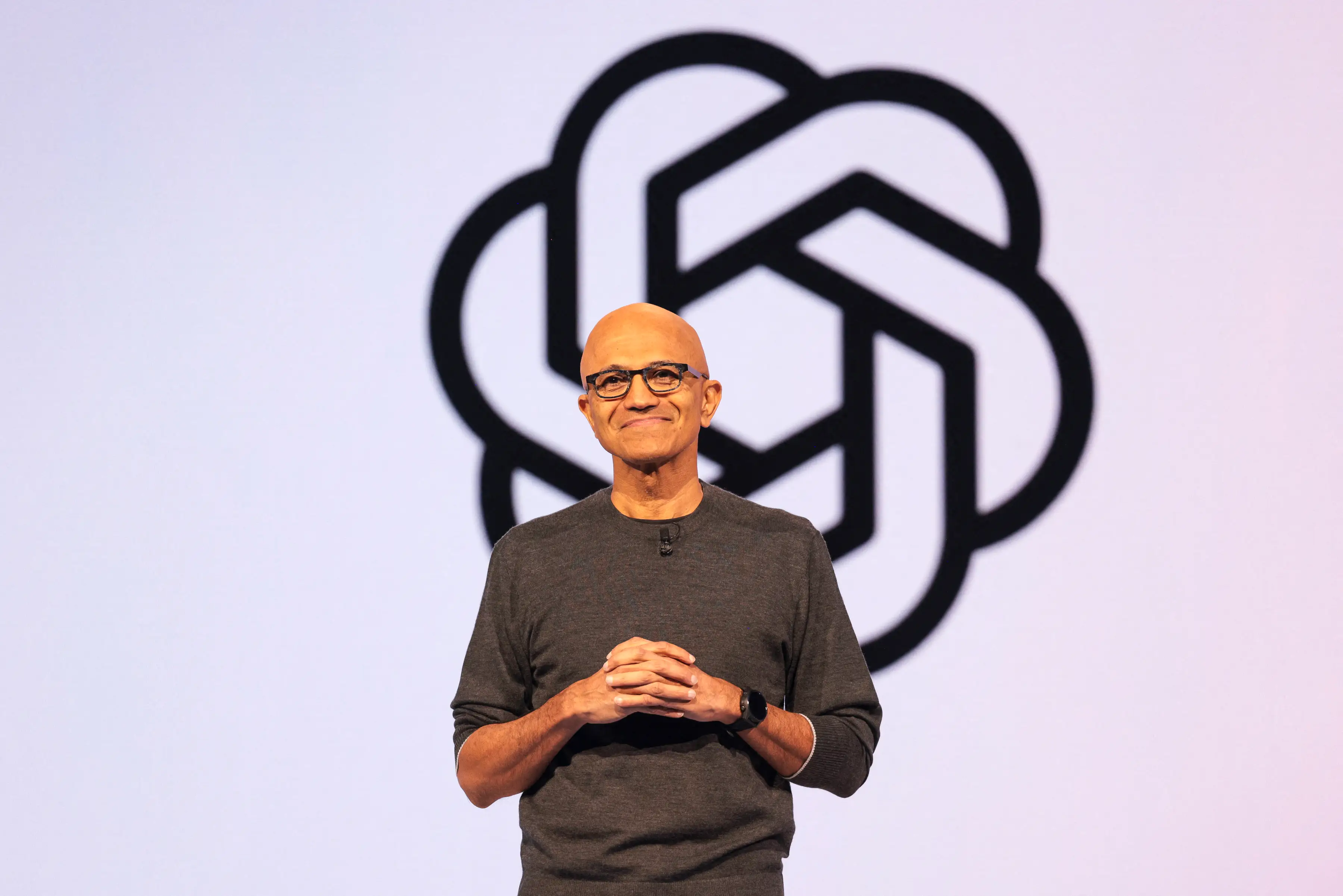 Satya Nadella is speaking in front of an OpenAI logo.