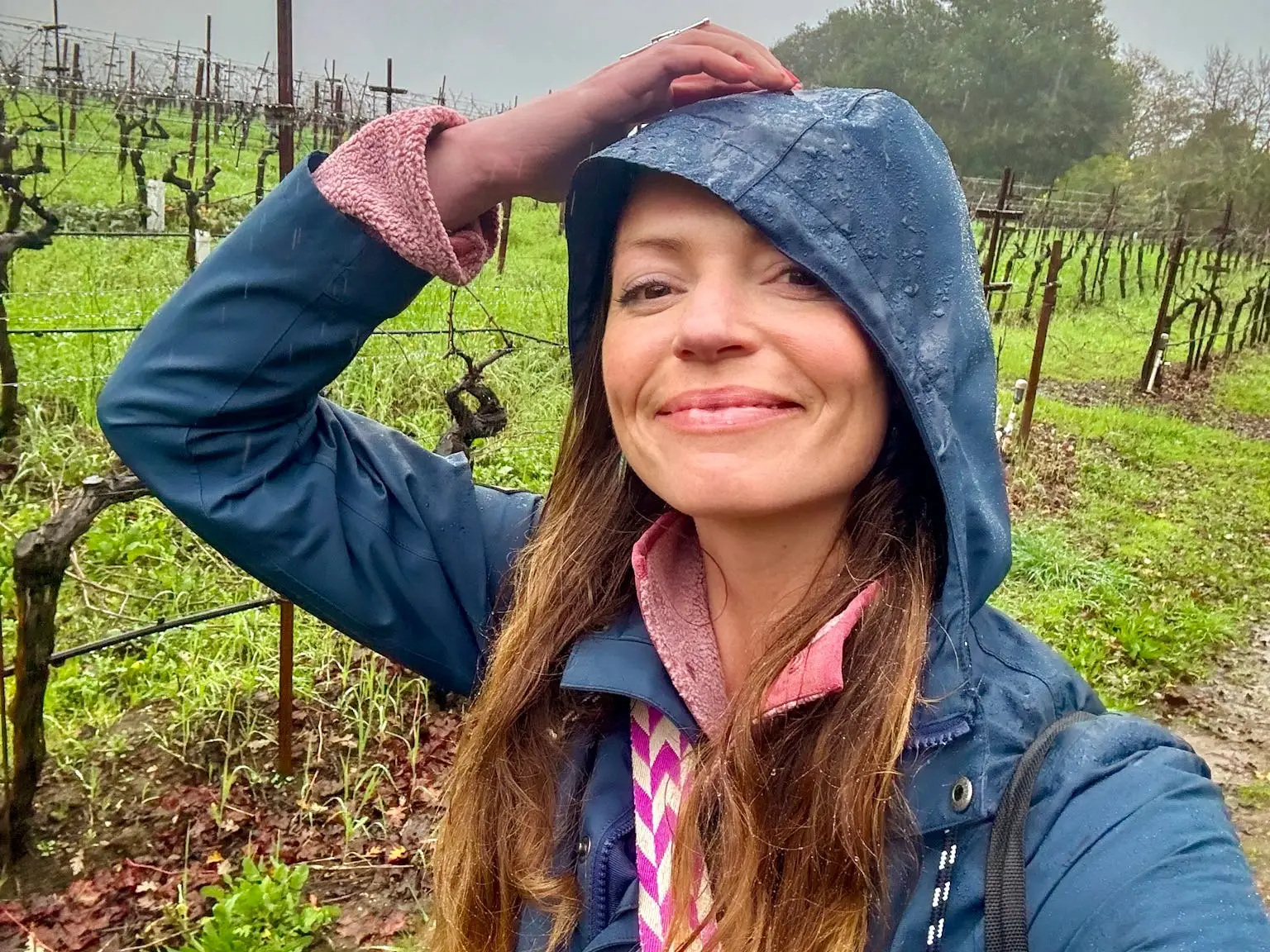Emily taking a selfie wearing a raincoat in a vineyard.