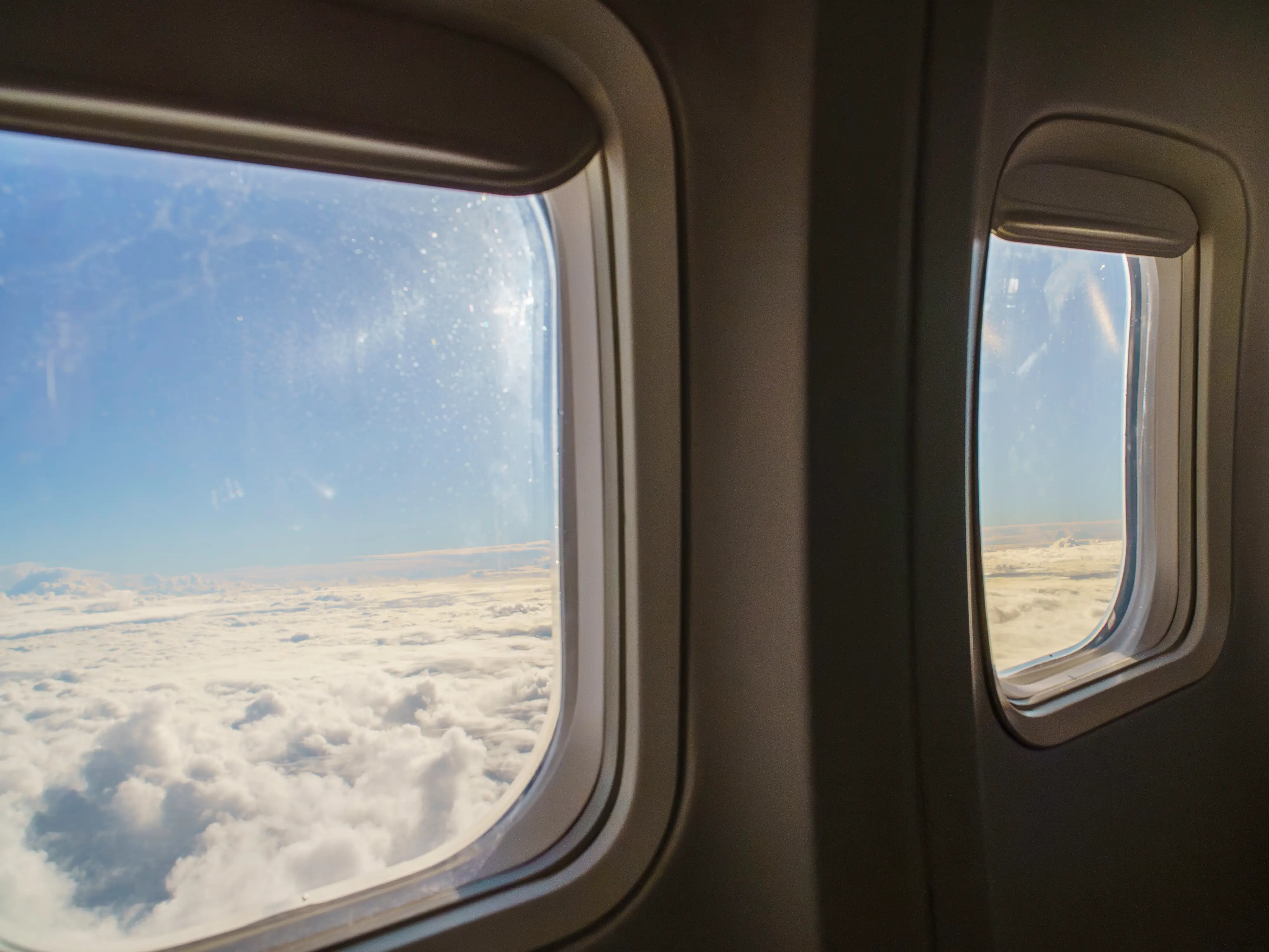 Two open plane windows show clouds and blue skies