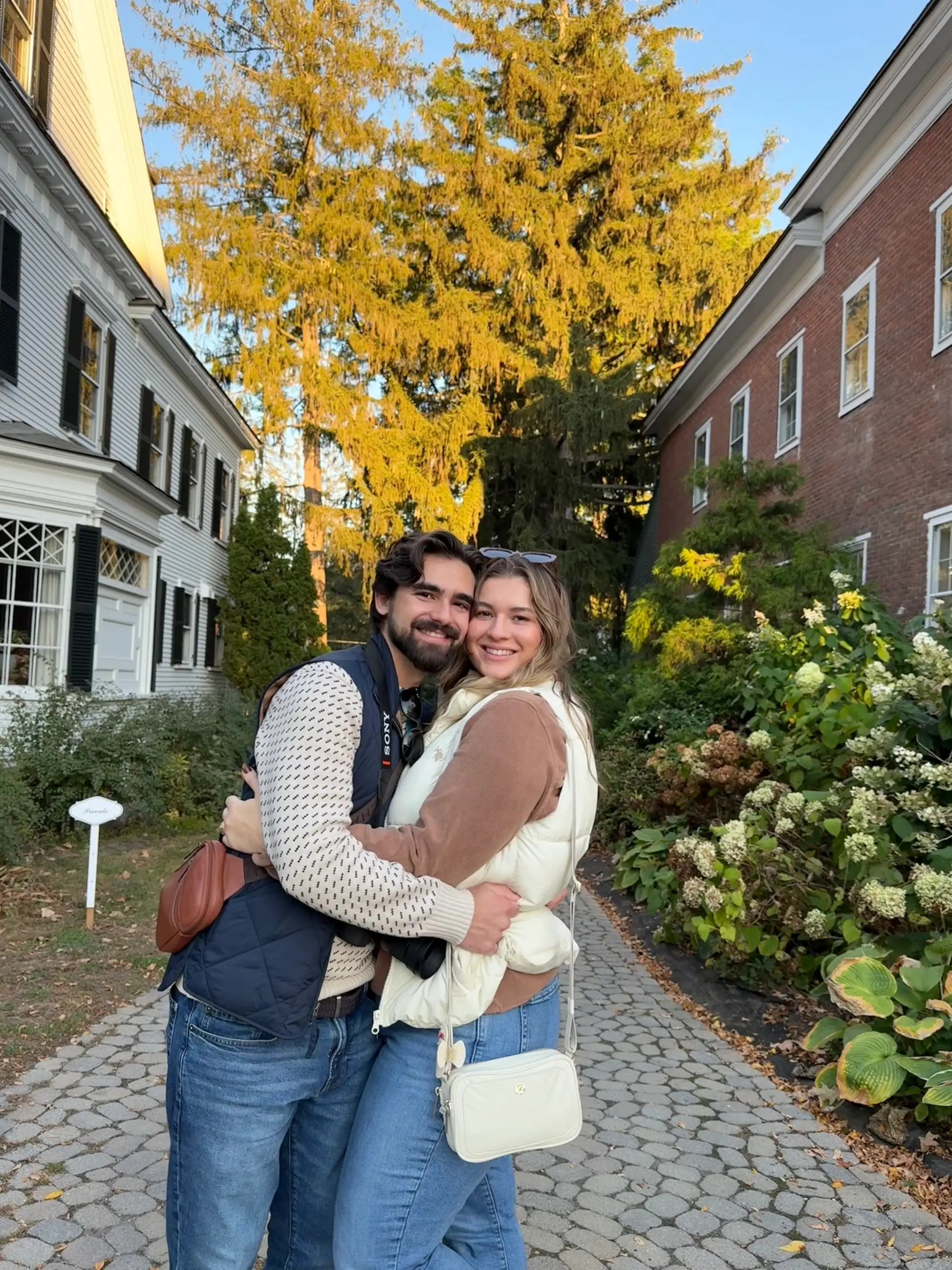 A couple embraces between two buildings with flowers nearby.