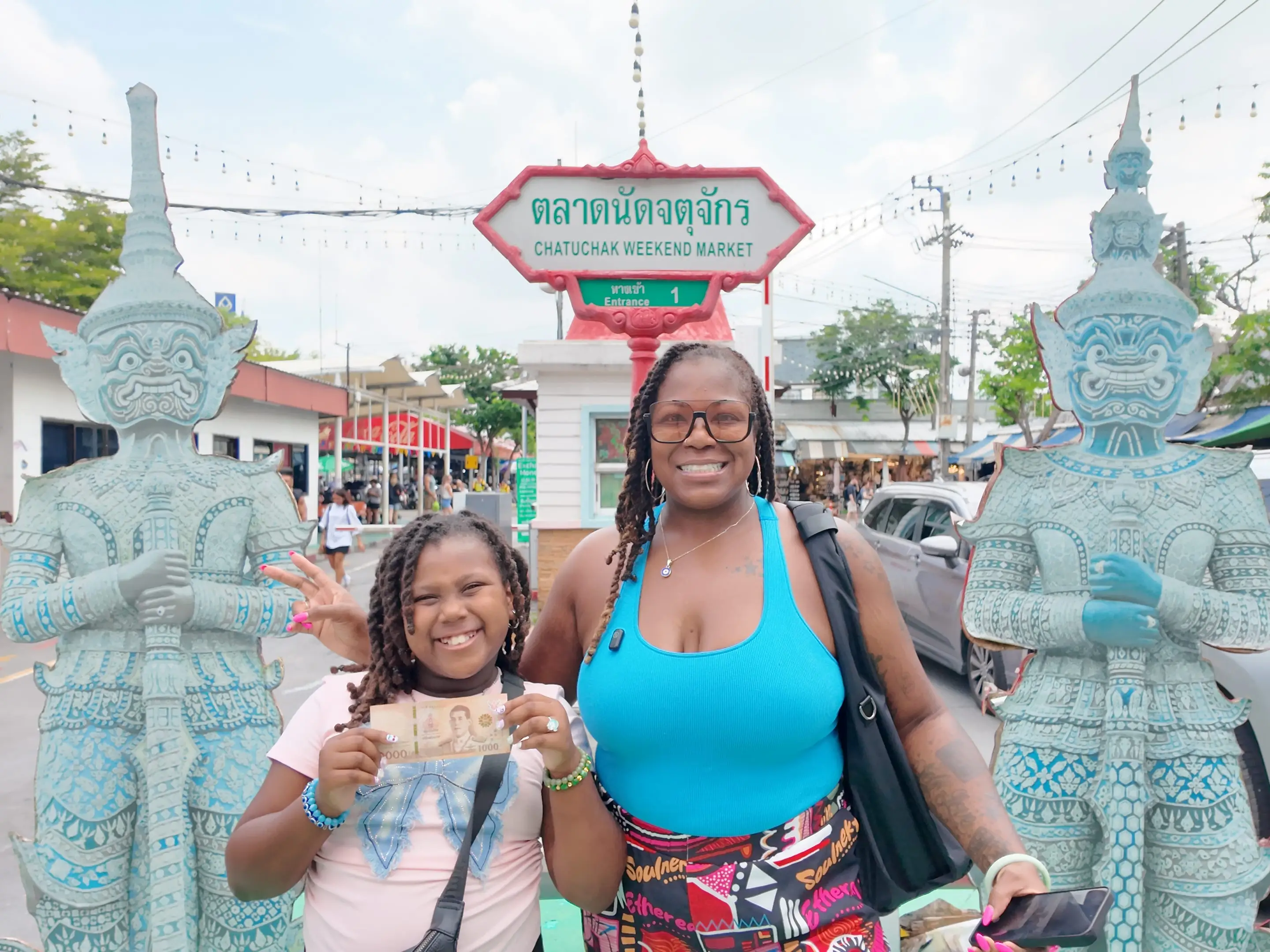 A woman and her daughter posing in front of a sign of Chatuchak market in Bangkok.