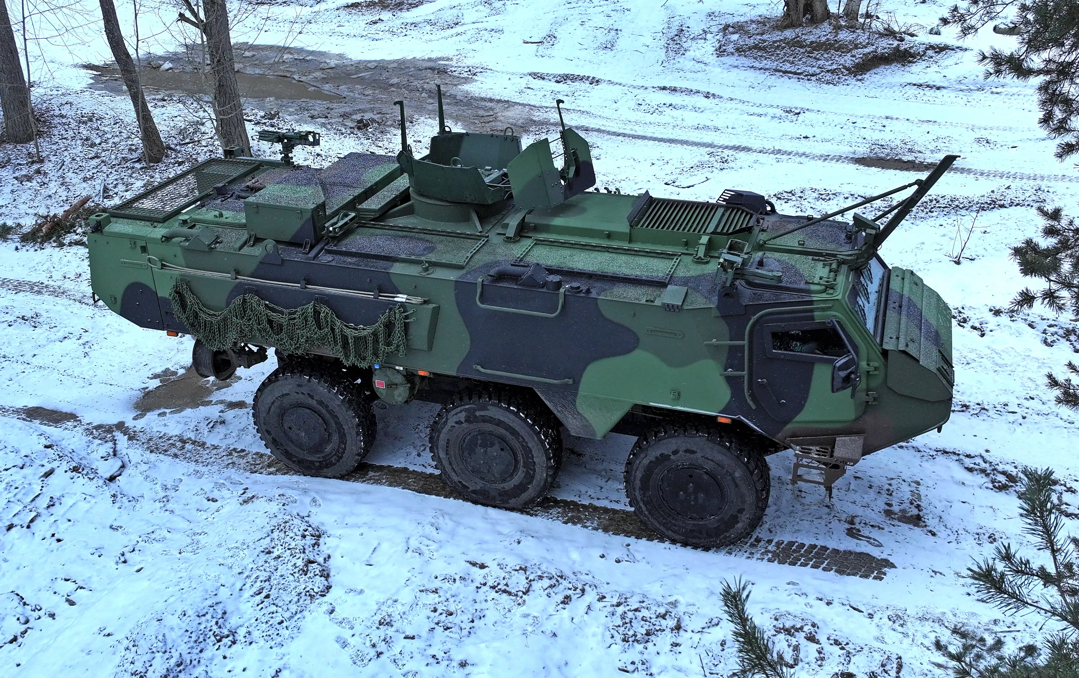 A Patria CAVS 6x6 is seen on a forest road with a thin layer of snow.