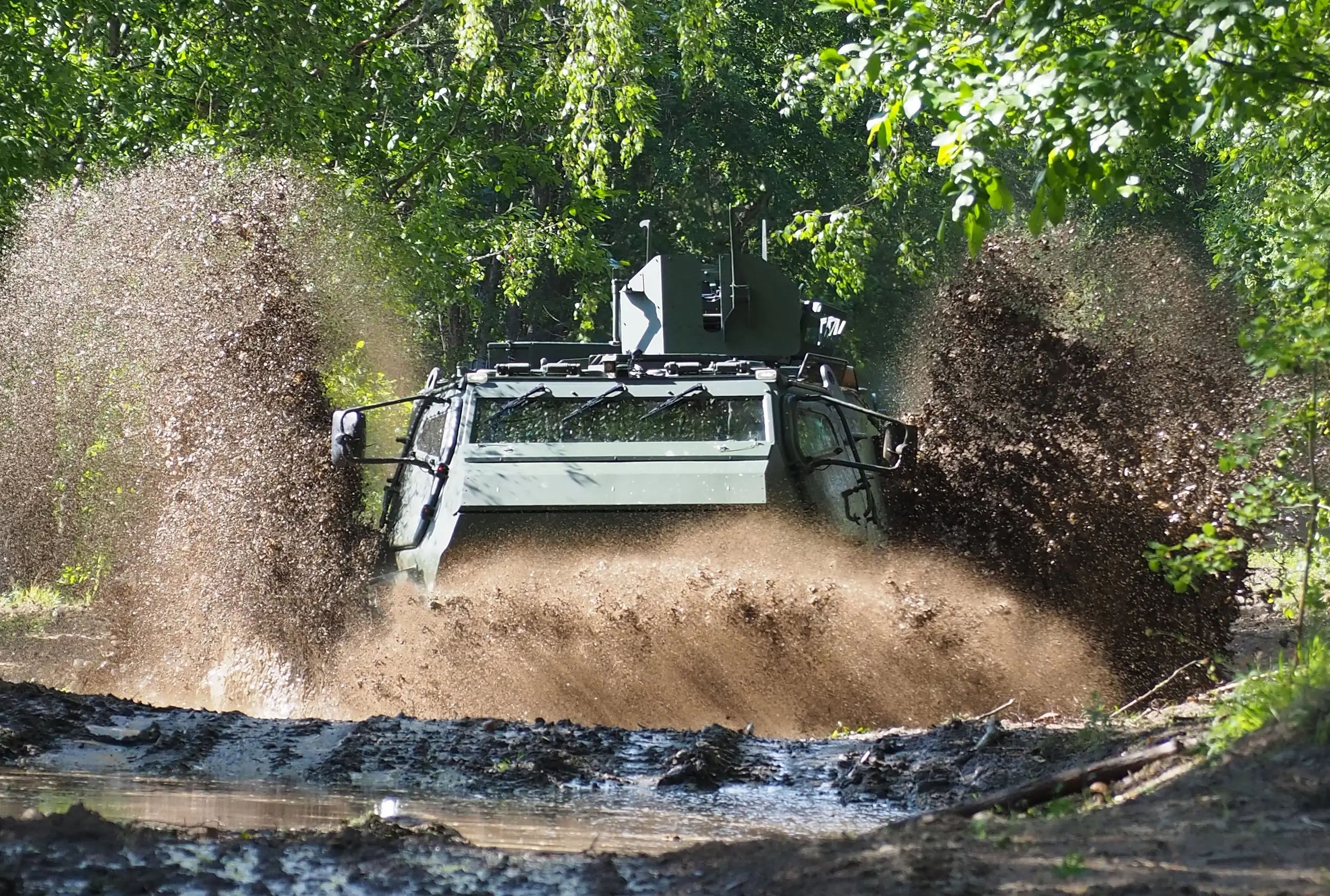 Patria's CAVS 6x6 kicks up mud as it navigates a wet road.