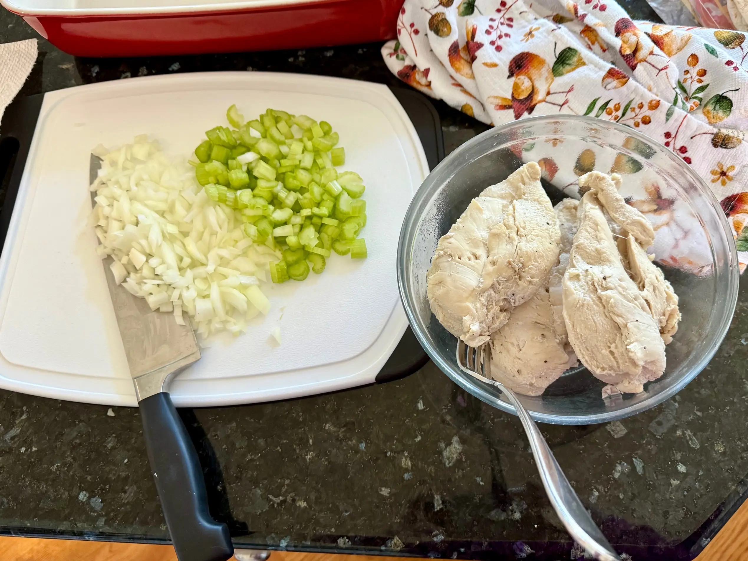 On the left, diced onion and celery on a cutting board. On the right, a bowl of poached chicken.