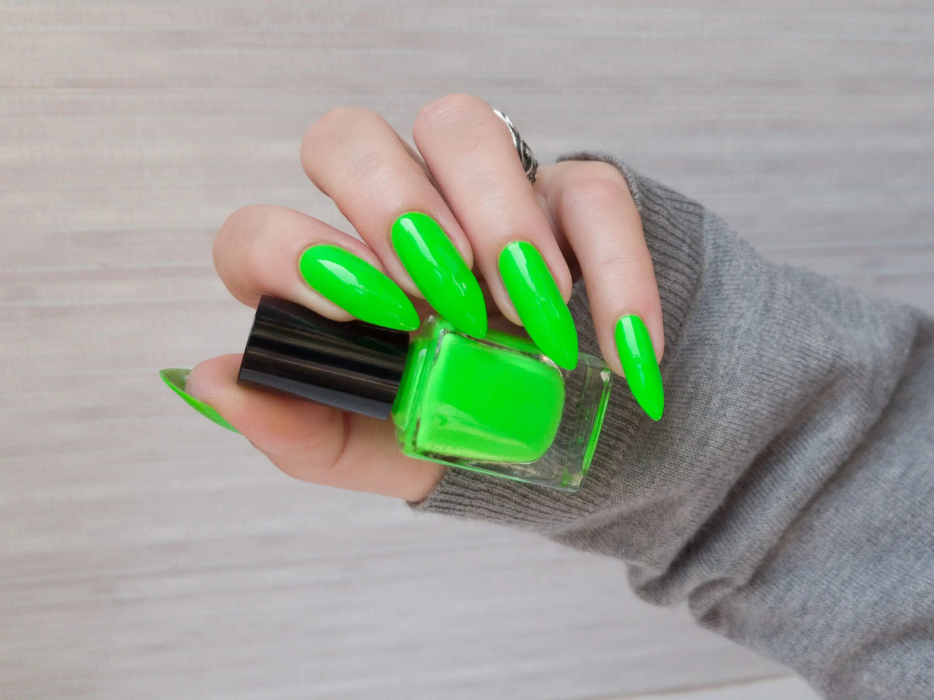 A woman's hand holding a neon-green bottle of nail polish, which matches her manicure.