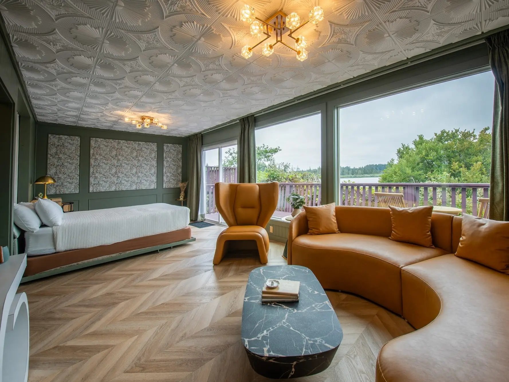 A hotel room with a textured ceiling, green walls, floral wallpaper, a white bed, an orange couch and chair, and a patio.