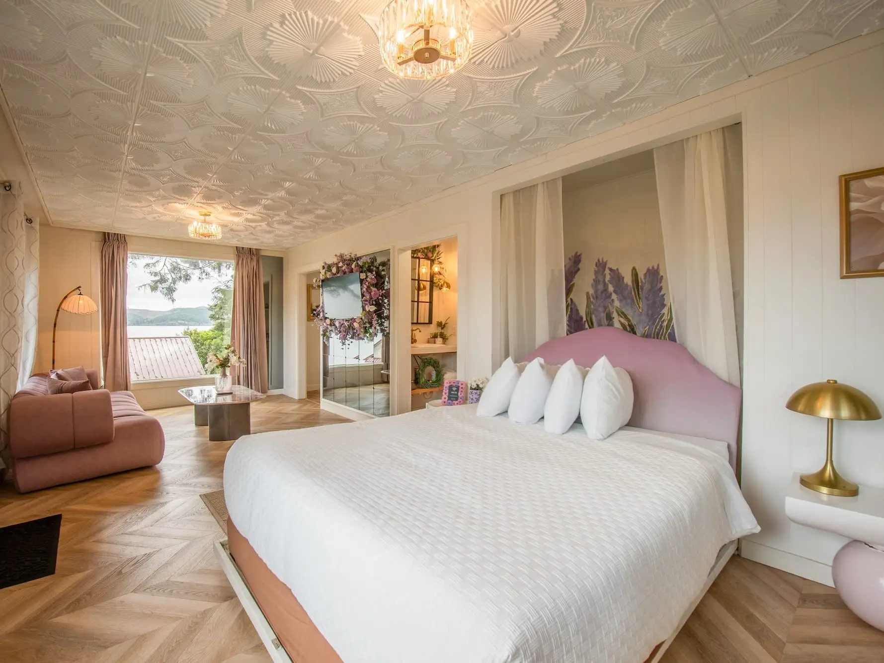 A hotel room with a pink couch and a Murphy bed with a purple headboard.