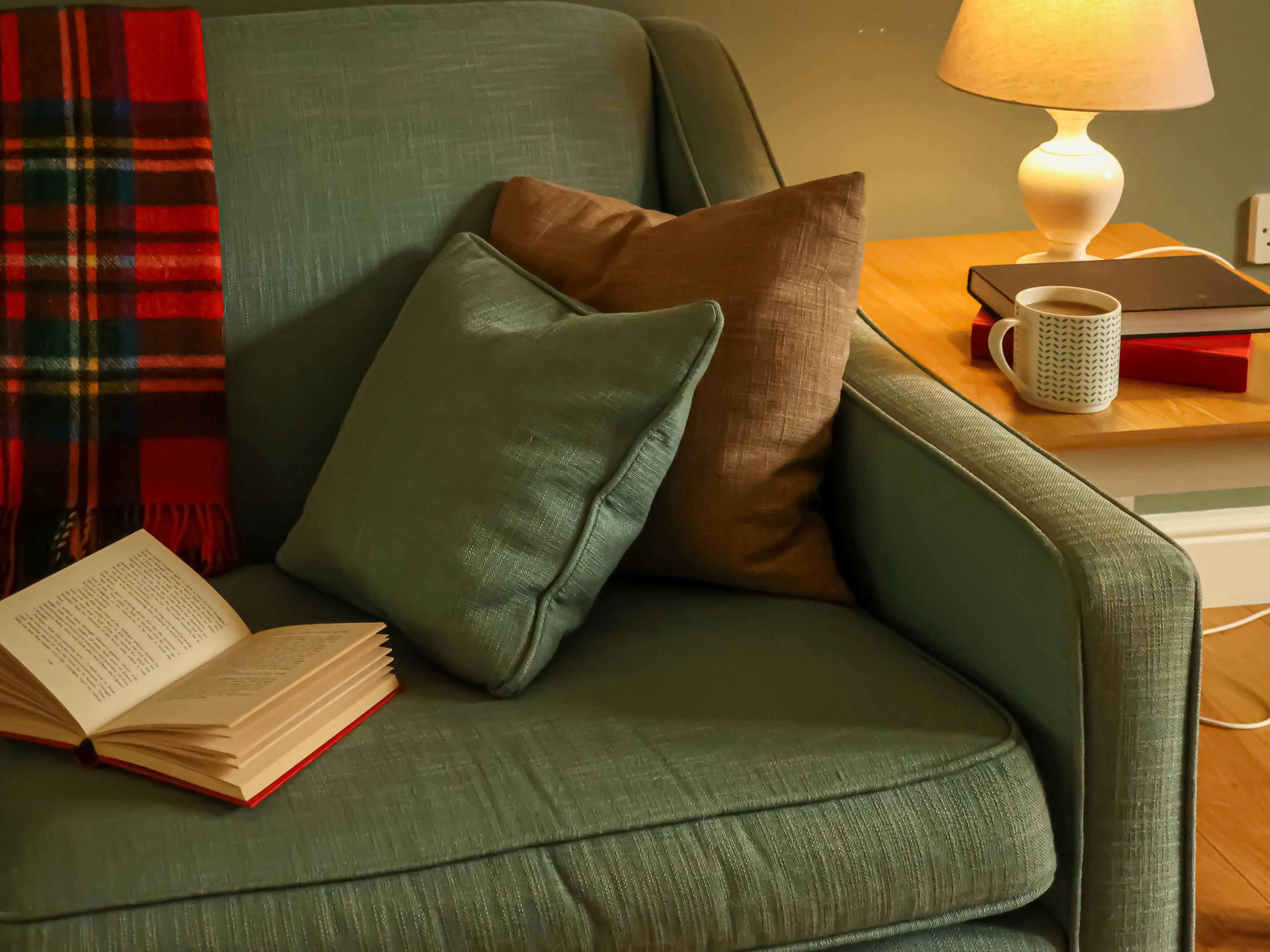 A green couch with a brown pillow and a cup of coffee.