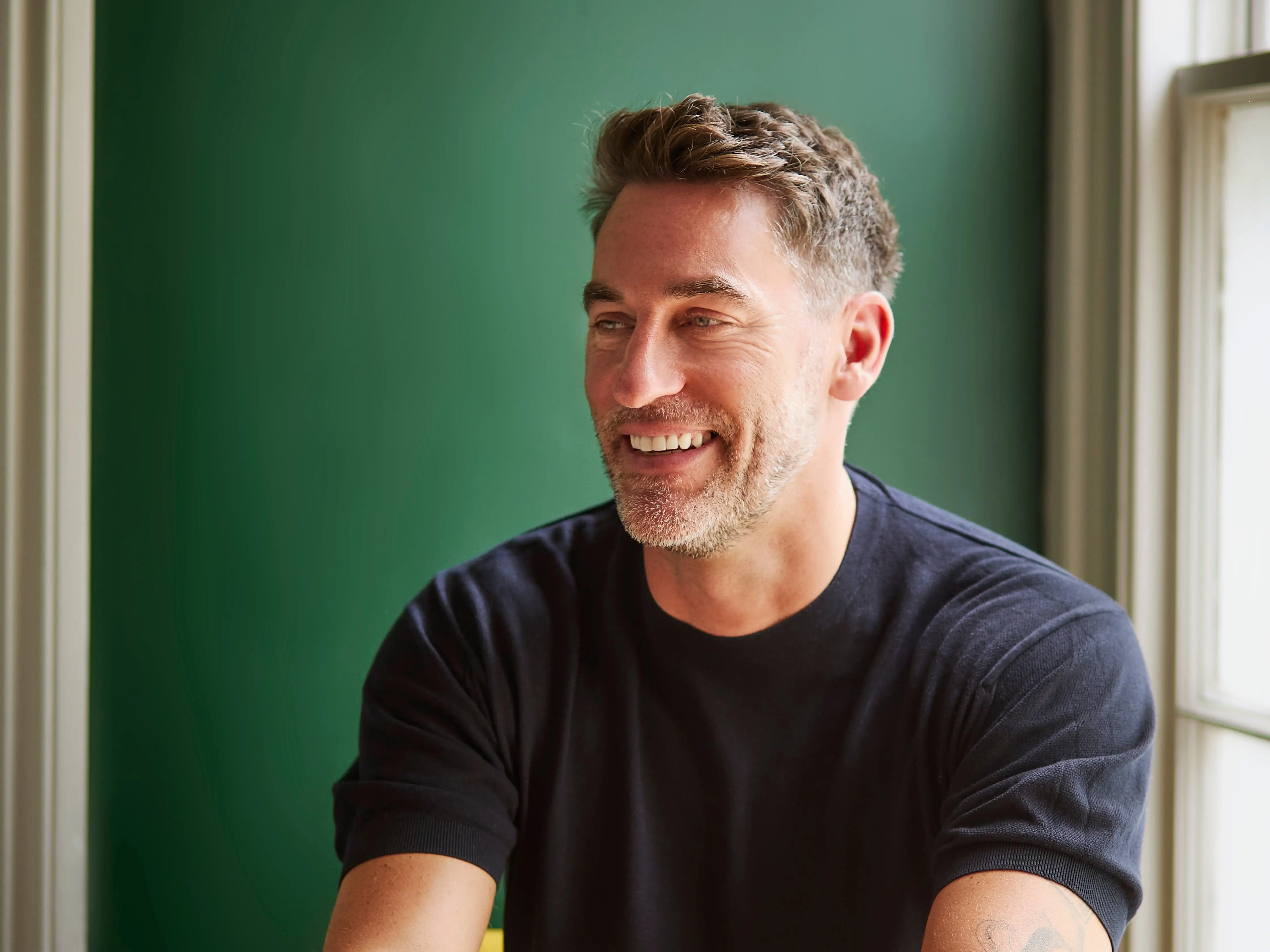 Rob Hobson sits at a table and smiles into the distance.