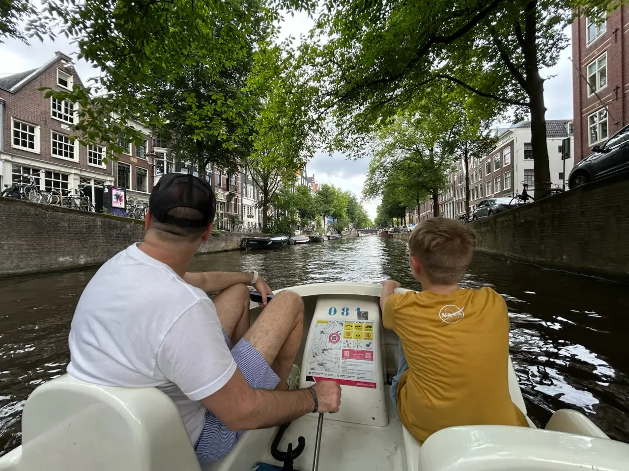 Man steering boat on canal with child sitting next to him