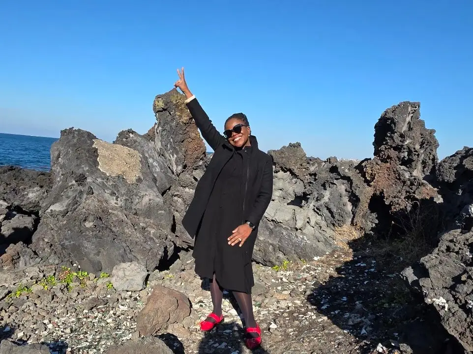 A woman posing on some rocks by the ocean.
