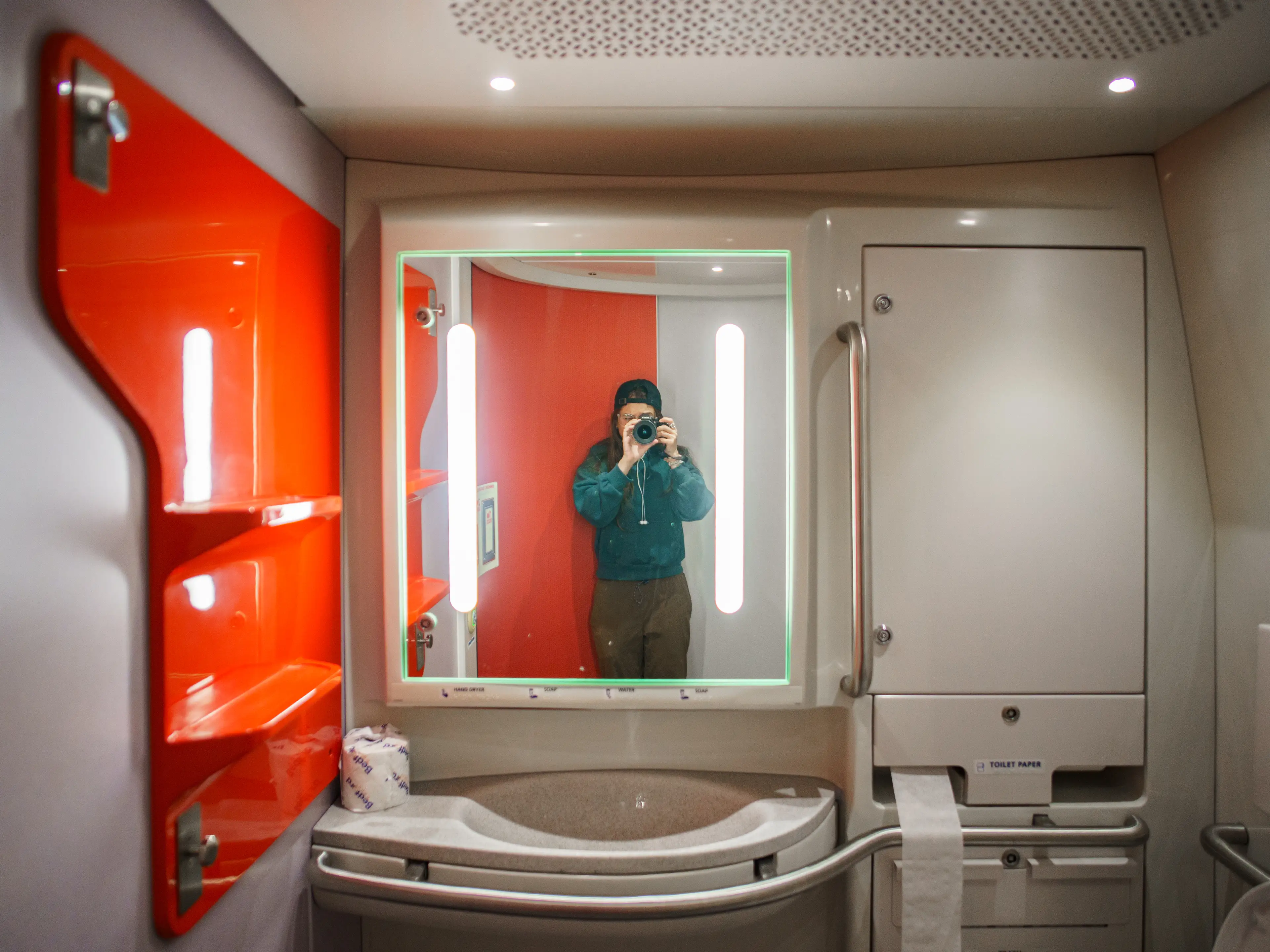 The author stands in front of a mirror in an Amtrak NextGen Acela train with a red shelf on the left