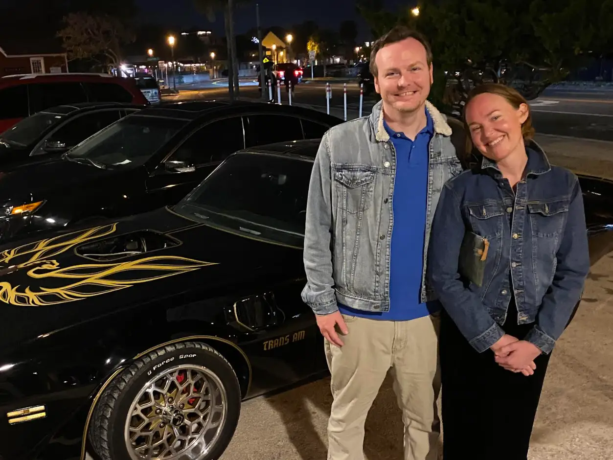 The writer and her husband standing in front of a car, wearing jean jackets.