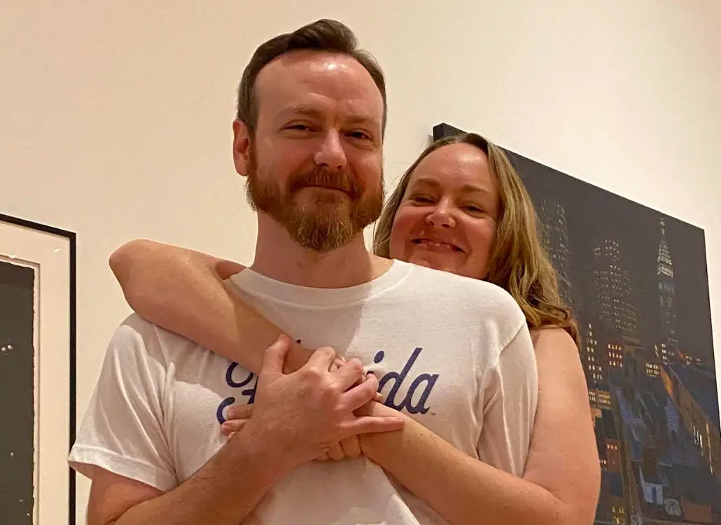 The writer posing with her husband in front of a painting.