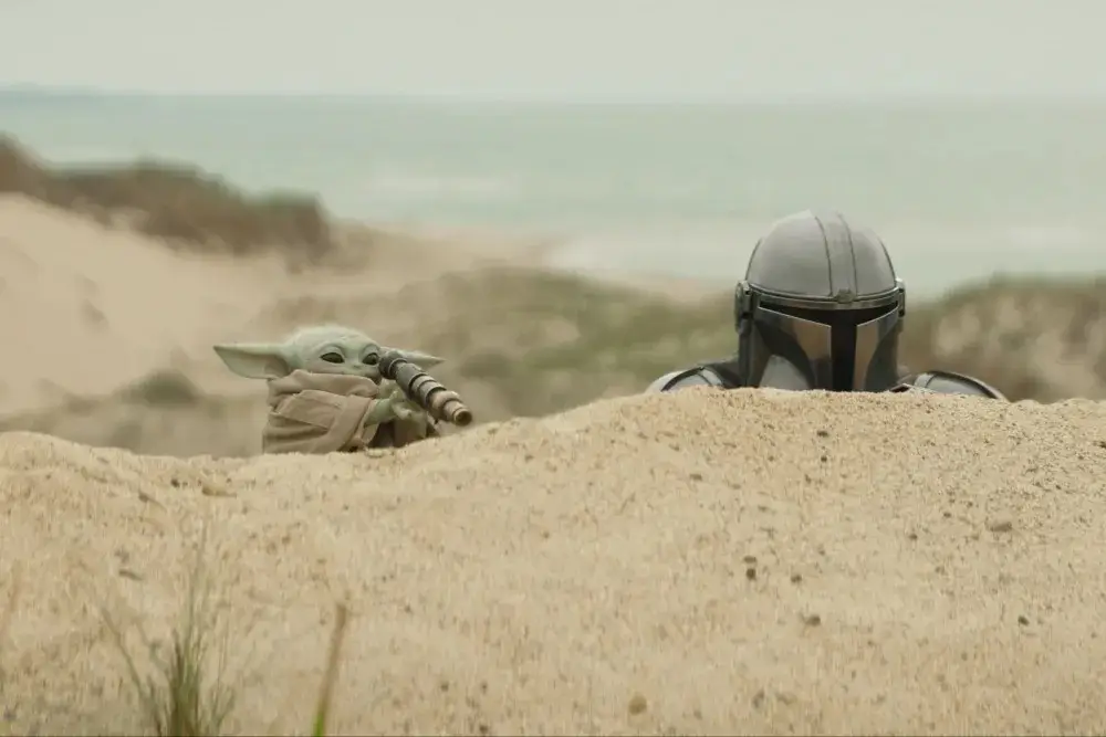 Mando and Grogu hiding behind a sane dune