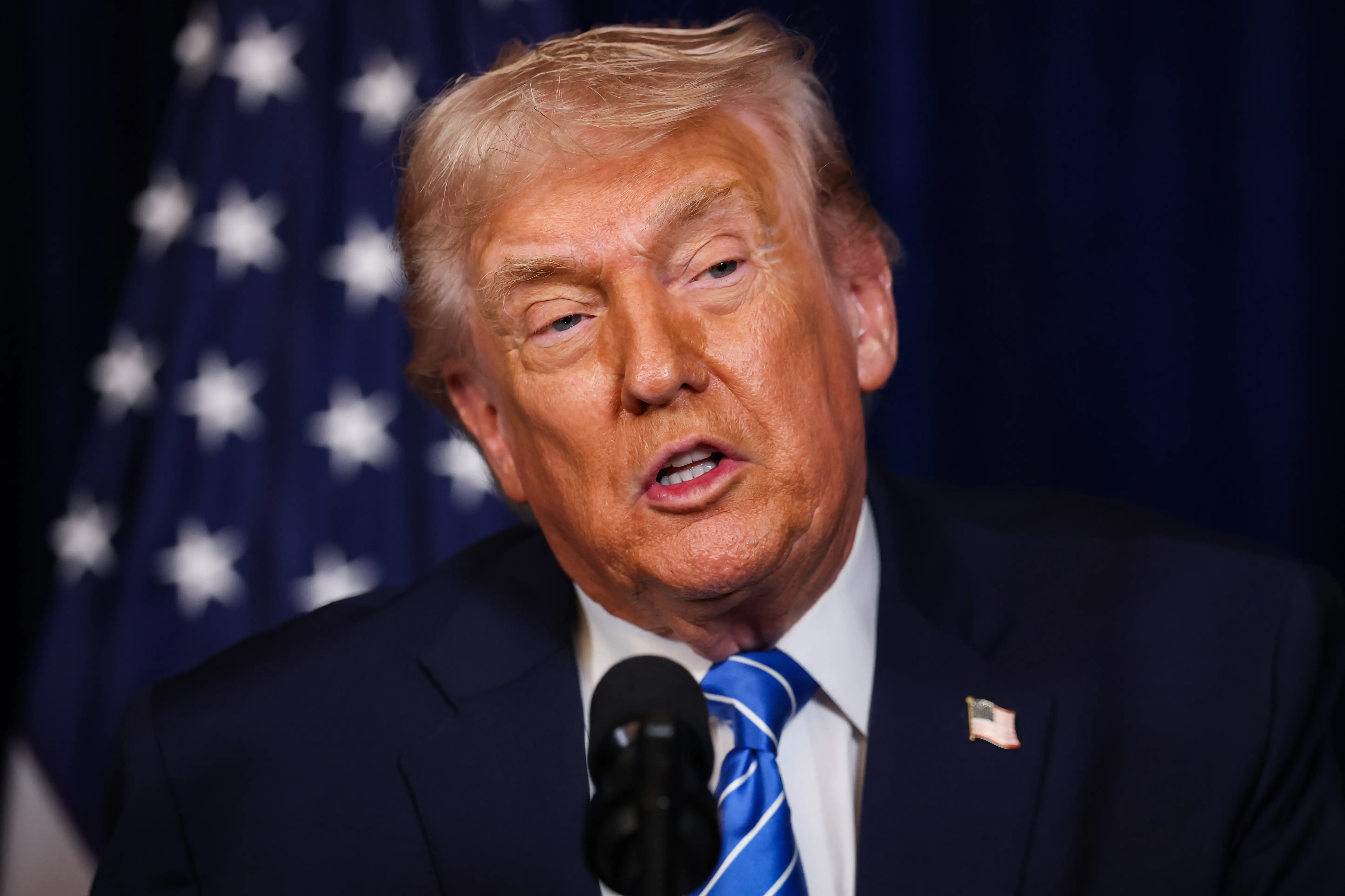 Donald Trump talks into a microphone in front of an American flag.