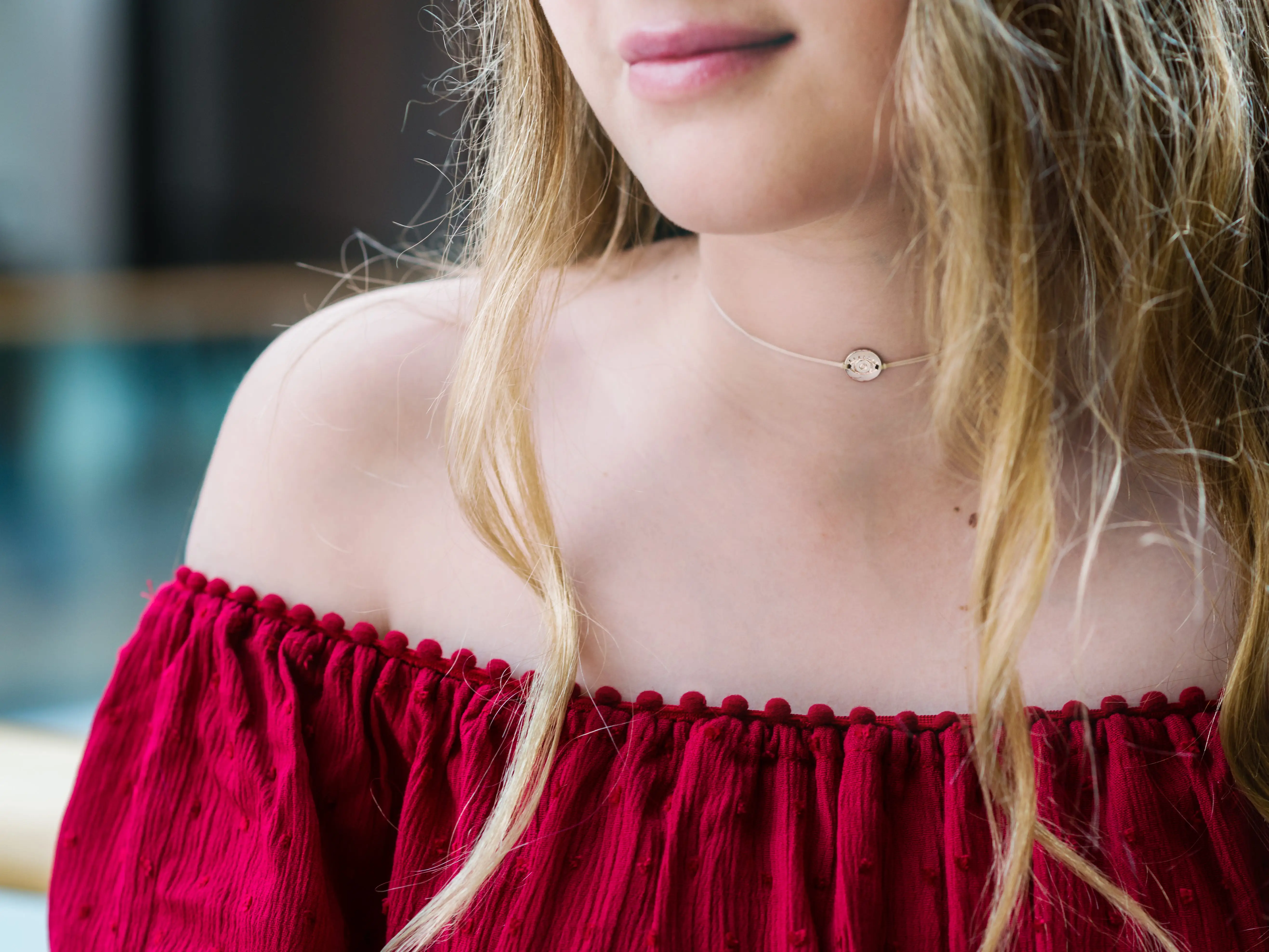 A woman wearing a thin chain around her neck and a red top.