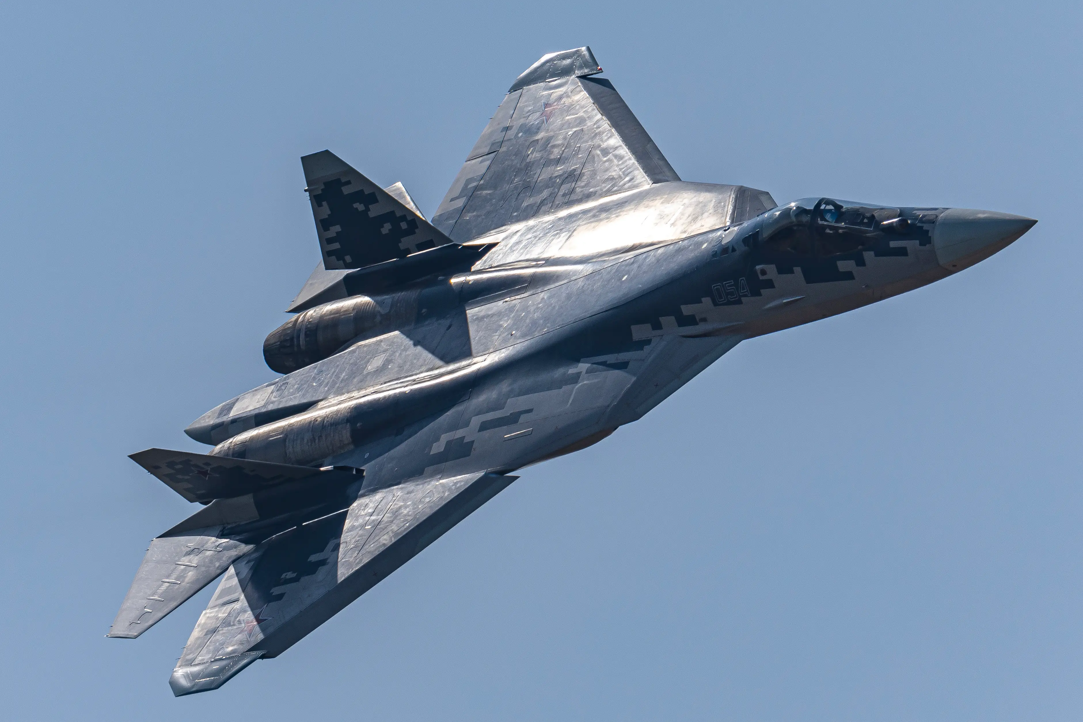 A grey fighter jet in a blue sky leaning slightly to one side