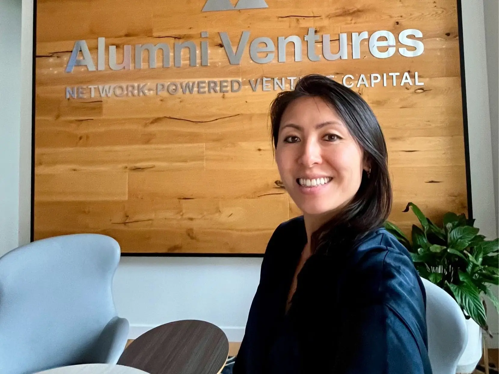 Sallie Jian smiles in front of a sign displaying the Alumni Ventures logo.