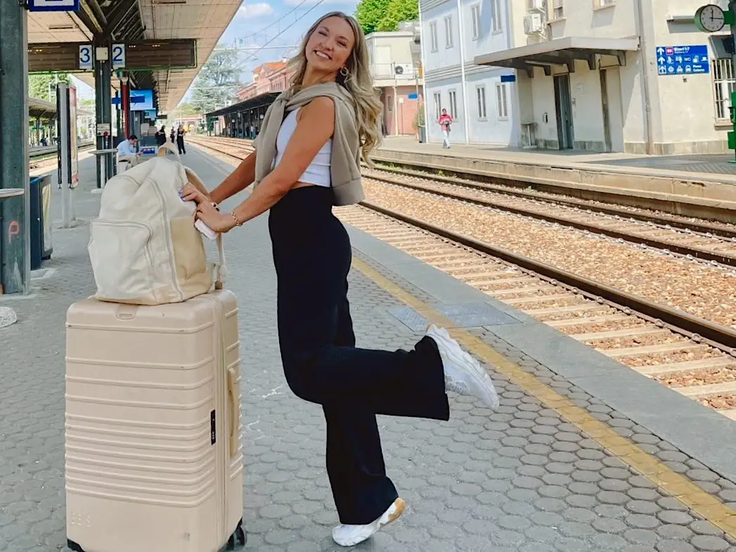 Chloe poses on a train platform with a suitcase and backpack.
