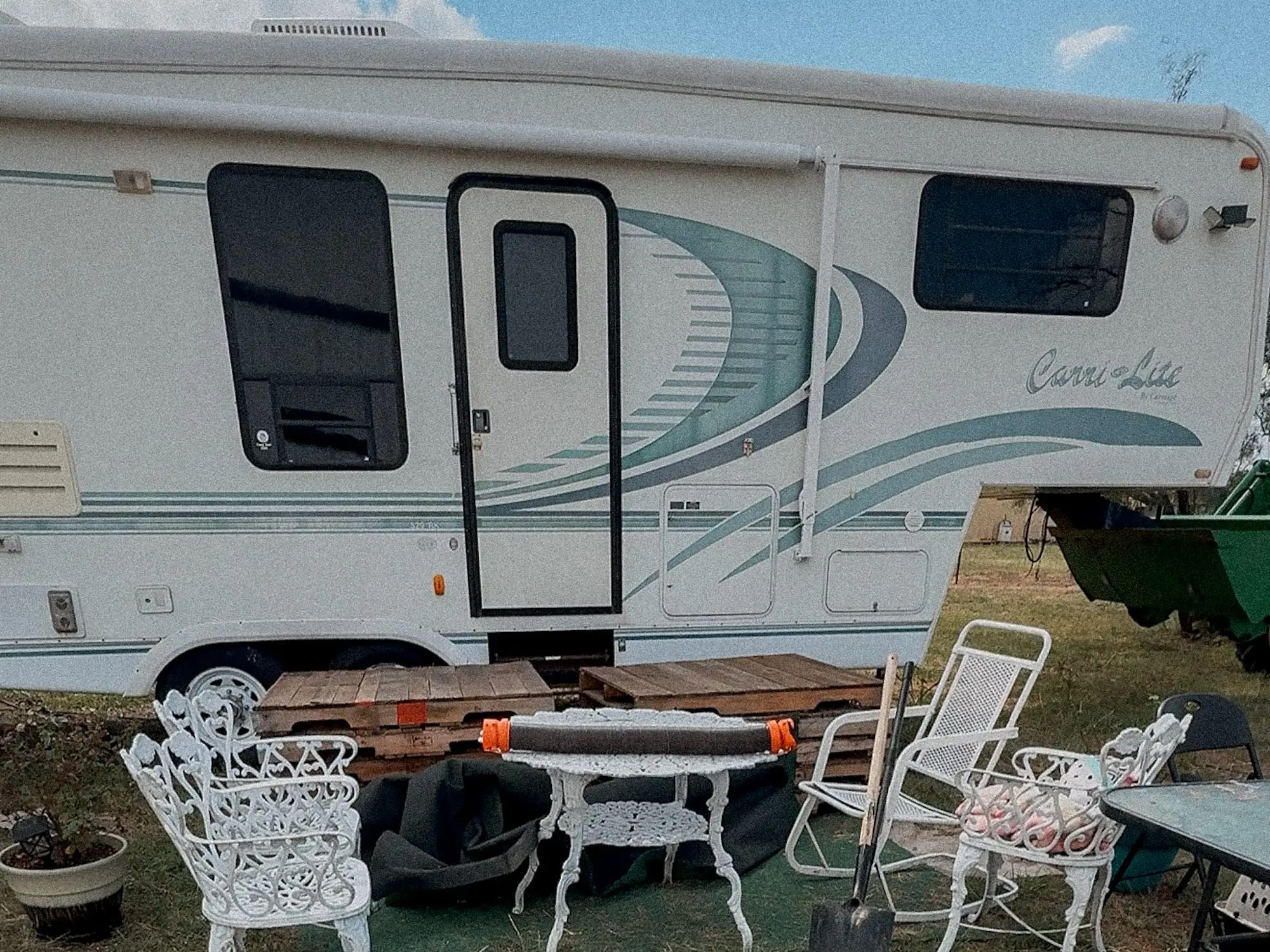 An RV sits in ayard with patio furniture in front of it.