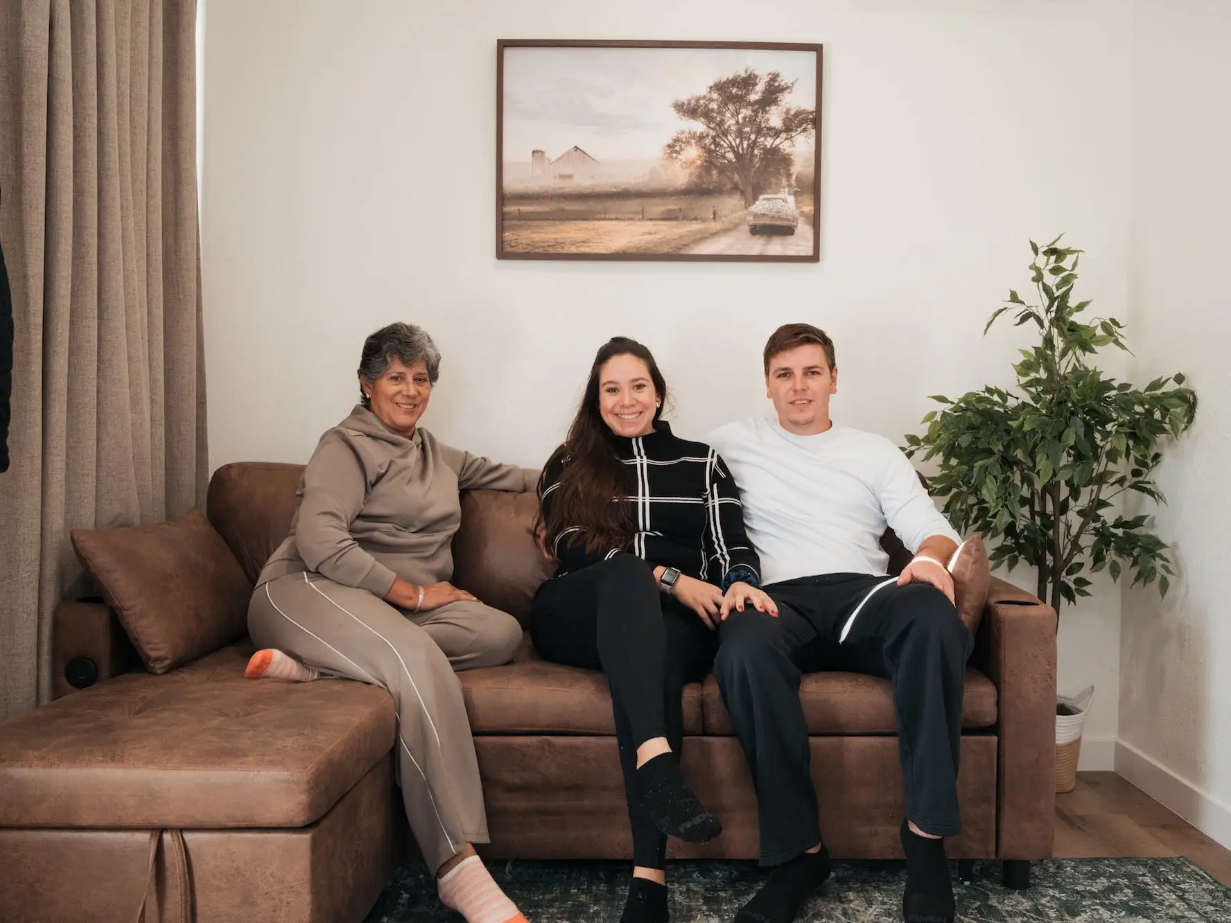 A mother sits on a couch with her daughter and son in-law.