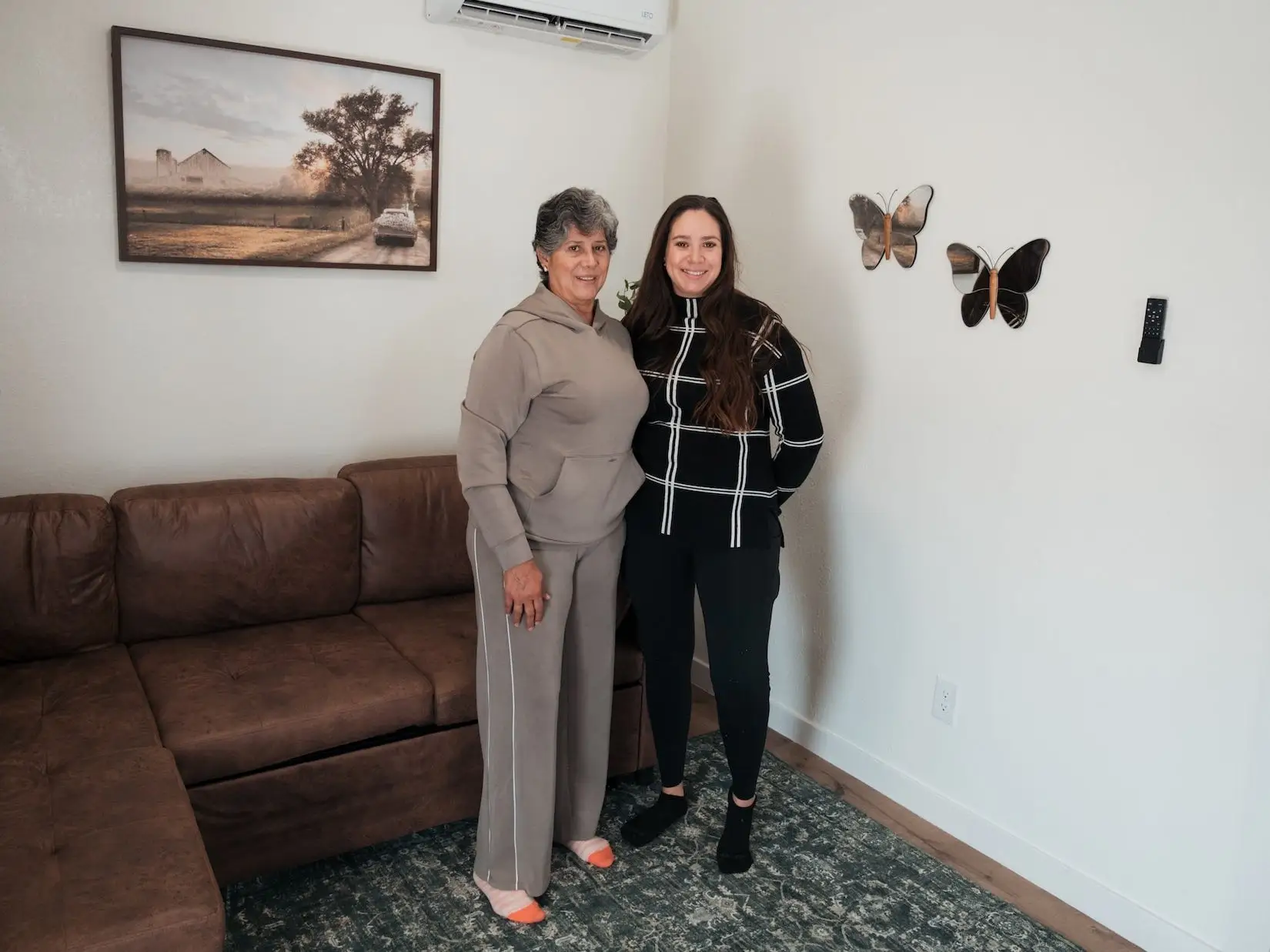 A mother and daughter stand together in a living area.