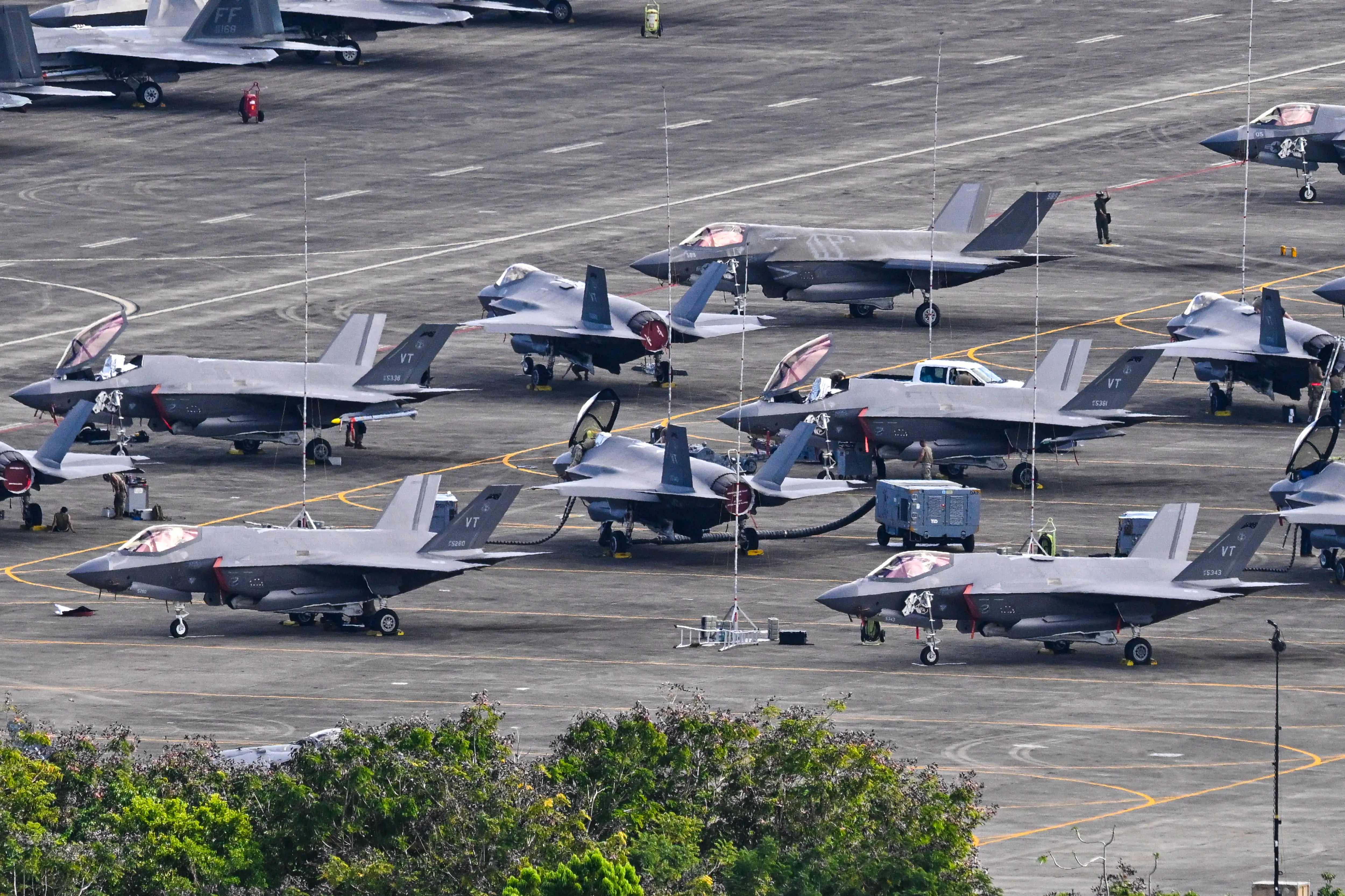 Groups of fighter jets sit on a tarmac.