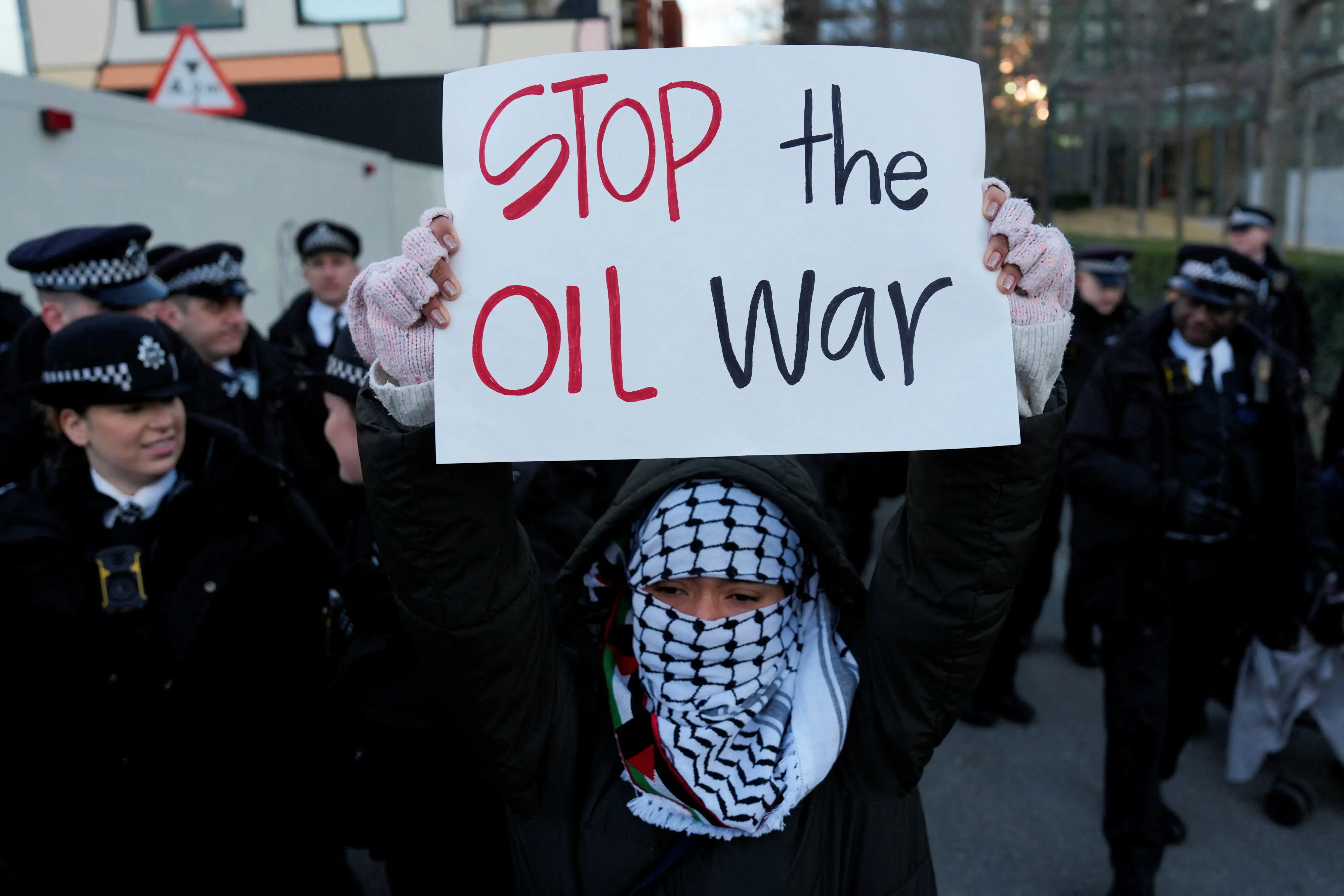 A woman wearing a hood and mask holds a sign that says, 