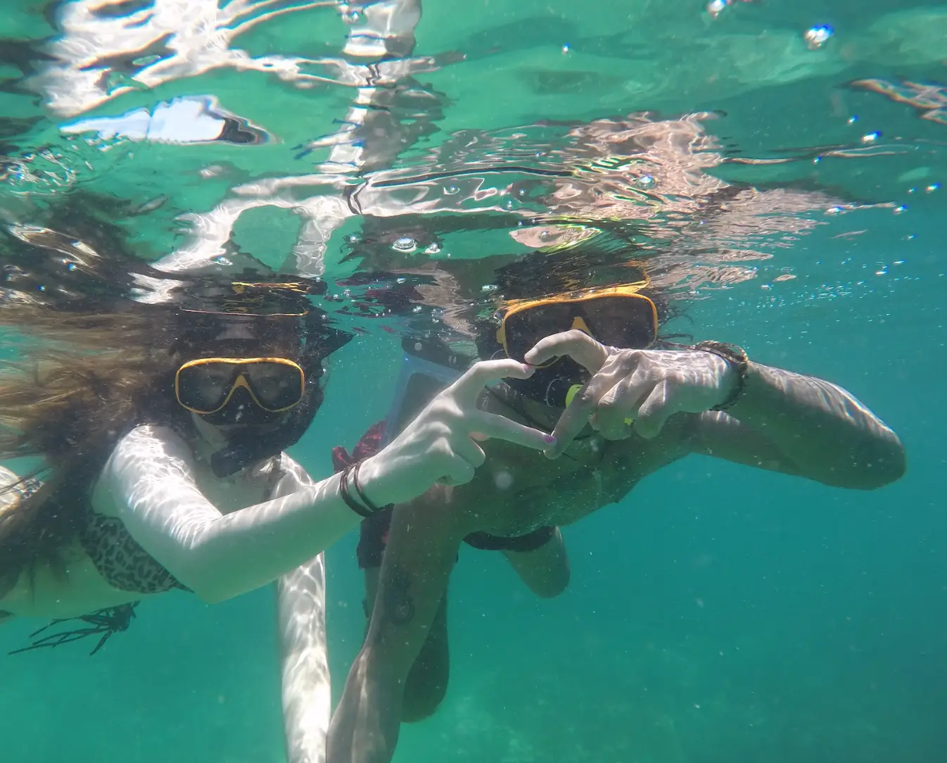The writer and her partner snorkeling and making a heart with their hands underwater.