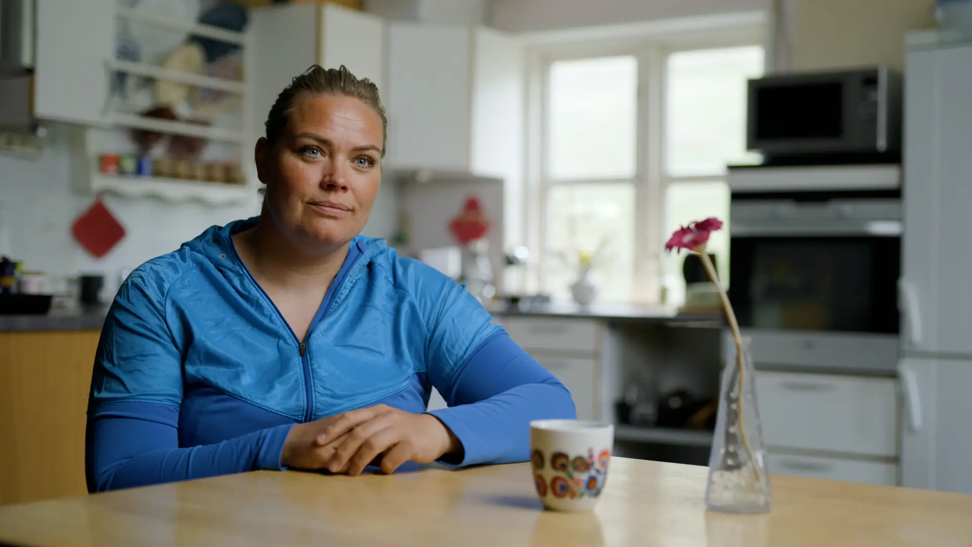 Tupaarnaq Kleist in a blue shirt at a kitchen table in her home.