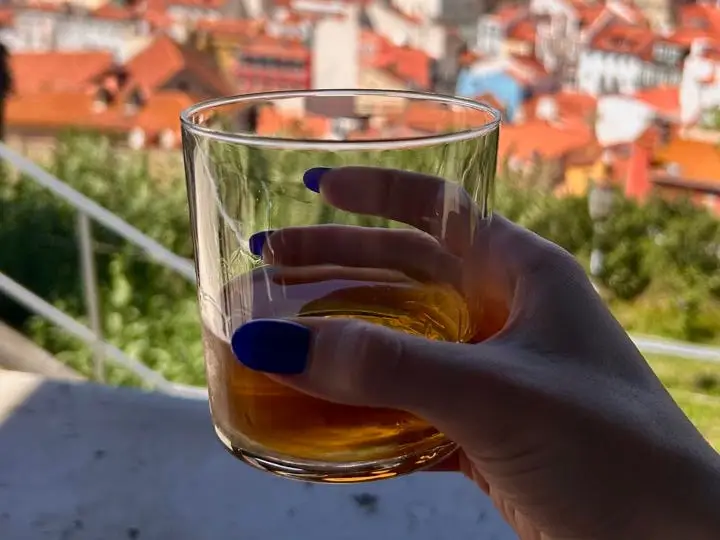 Hand holding drink in front of view of Portugal
