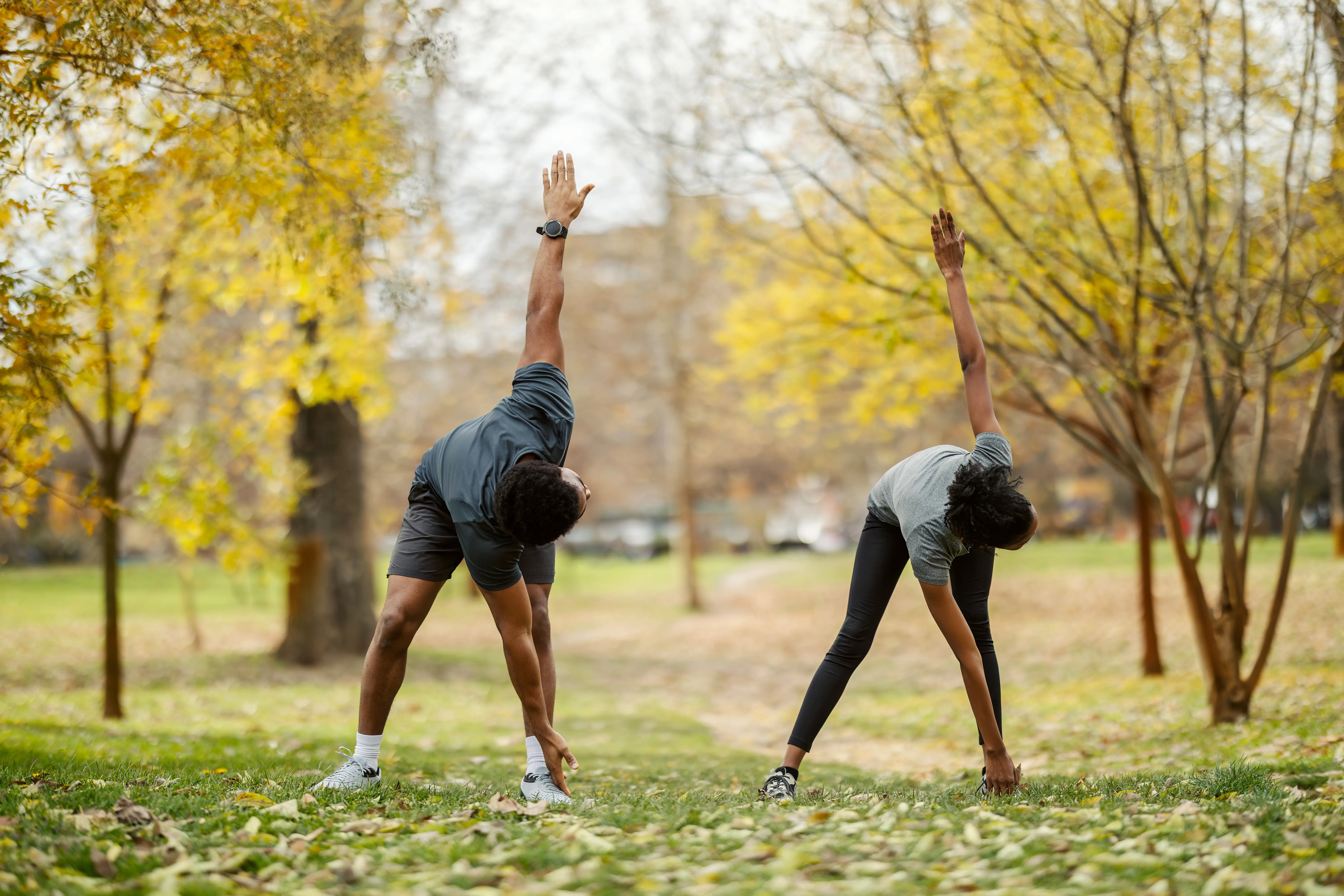 two people stretching and doing yoga in a public park